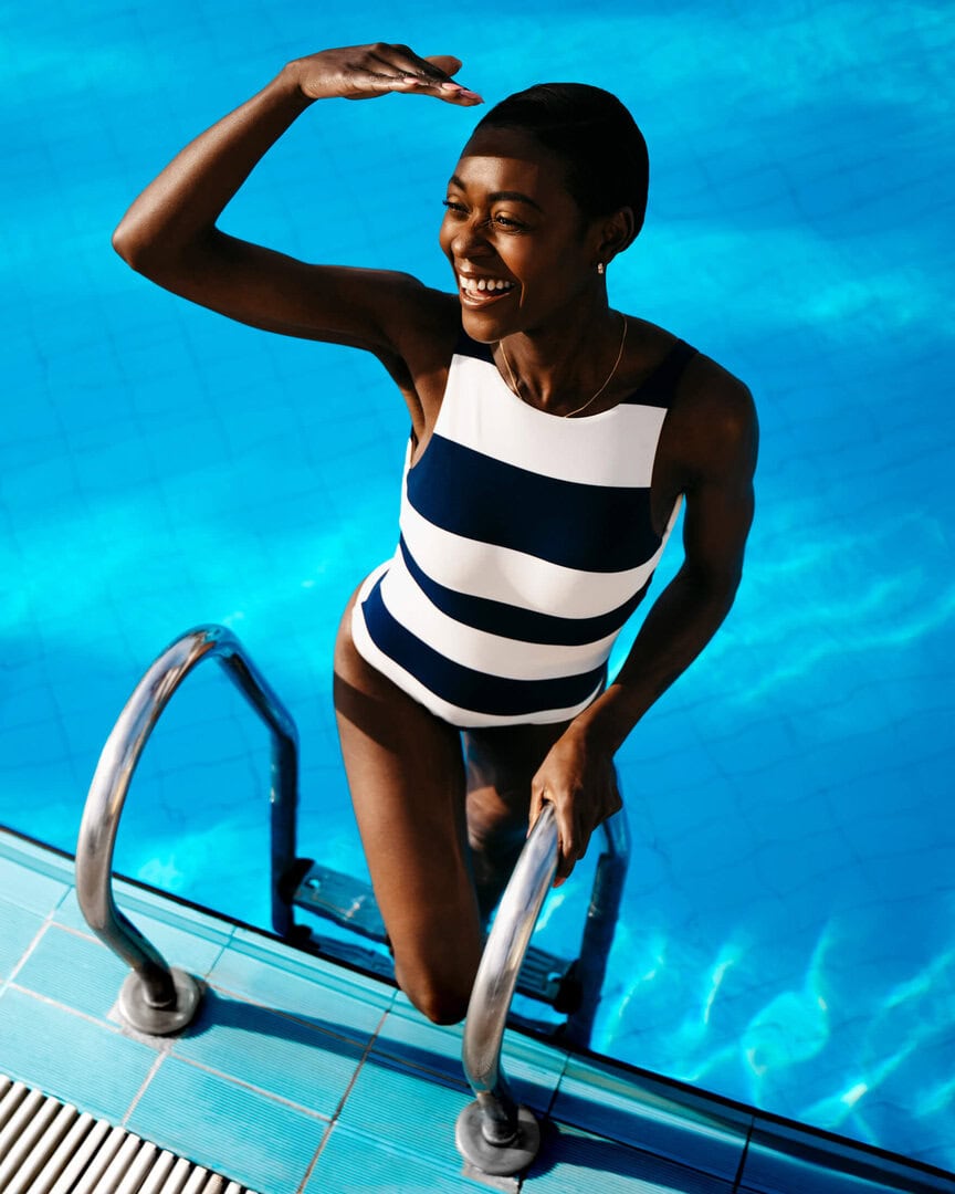 Woman in a black-and-white striped swimsuit at the edge of a blue pool