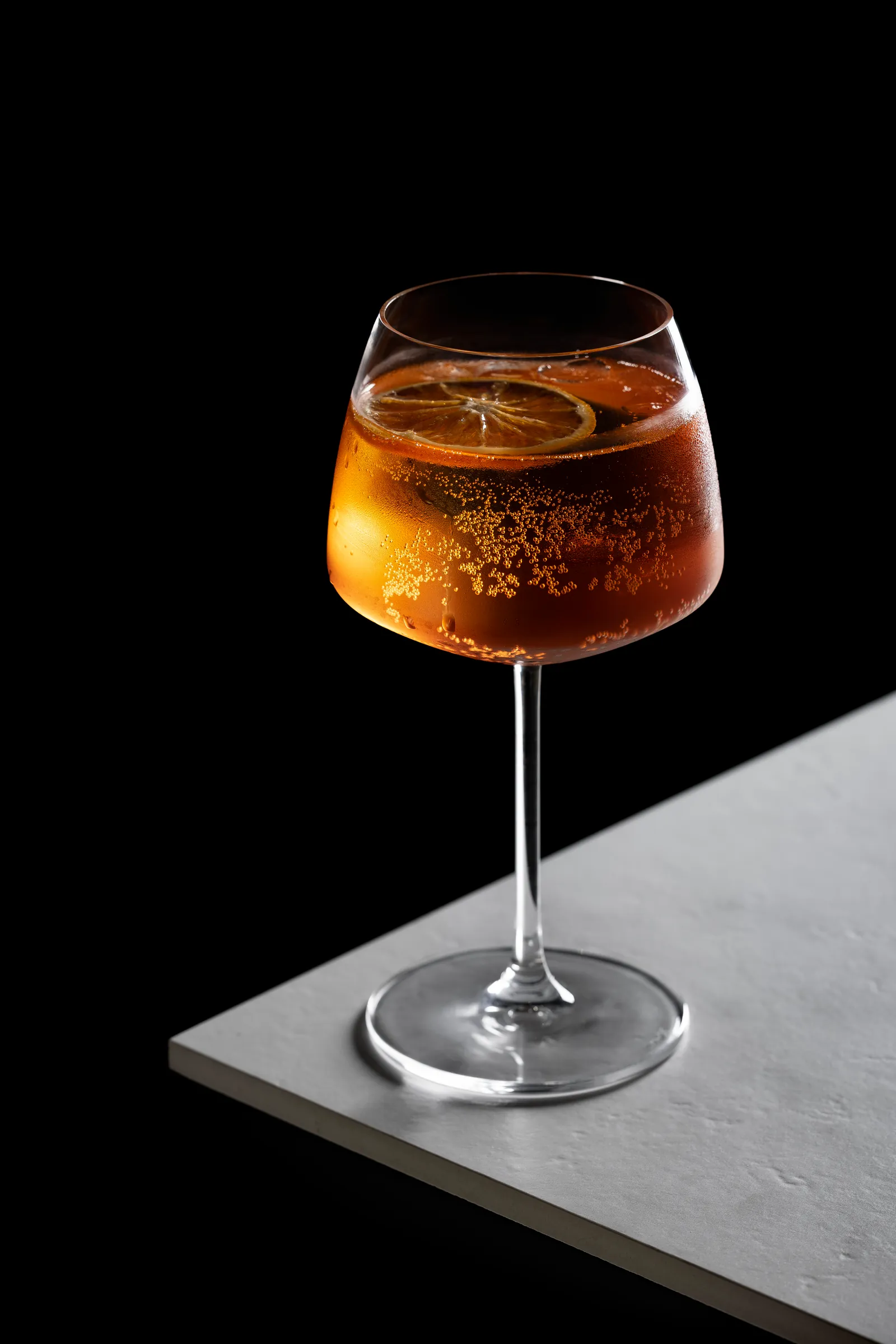 Amber spritz cocktail in a stemmed glass on a pale stone ledge