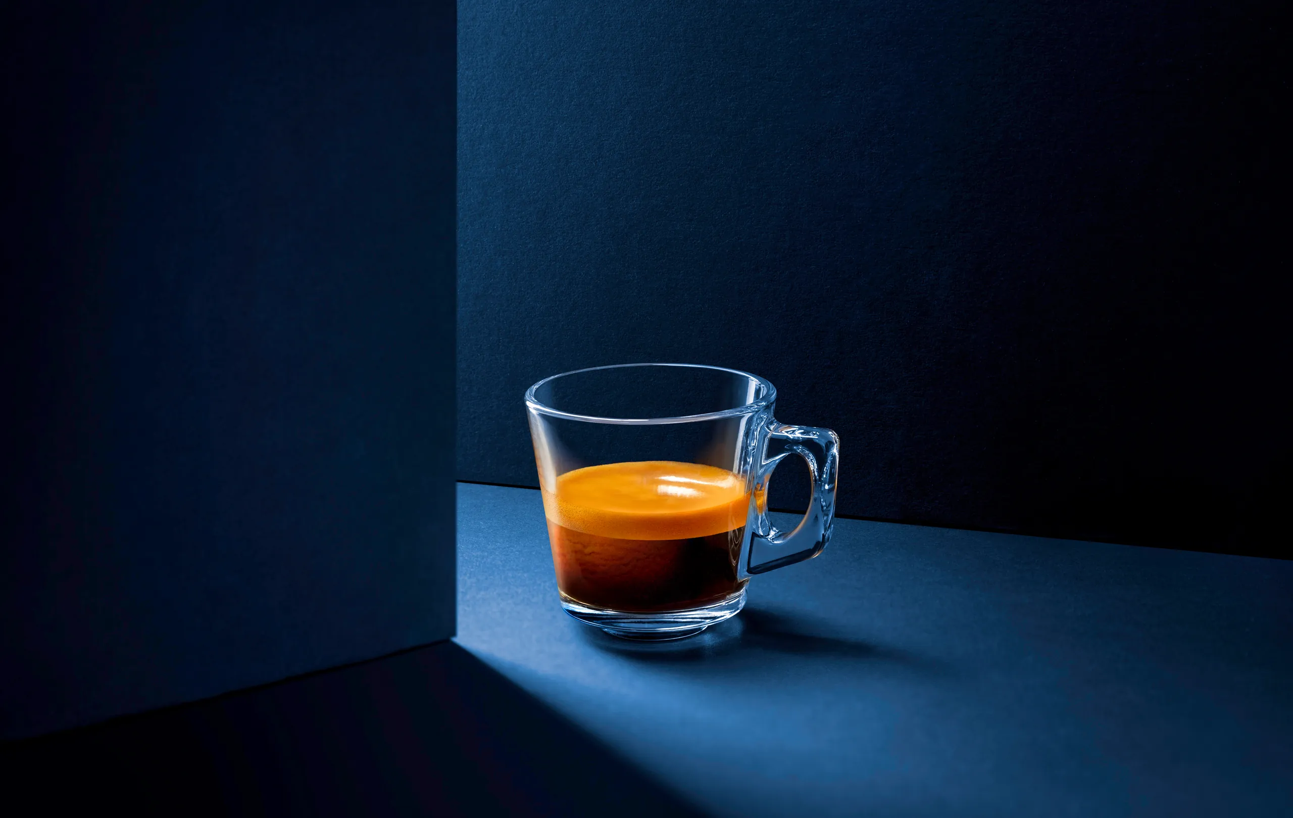 Glass cup of espresso on a dark blue surface in a pool of light