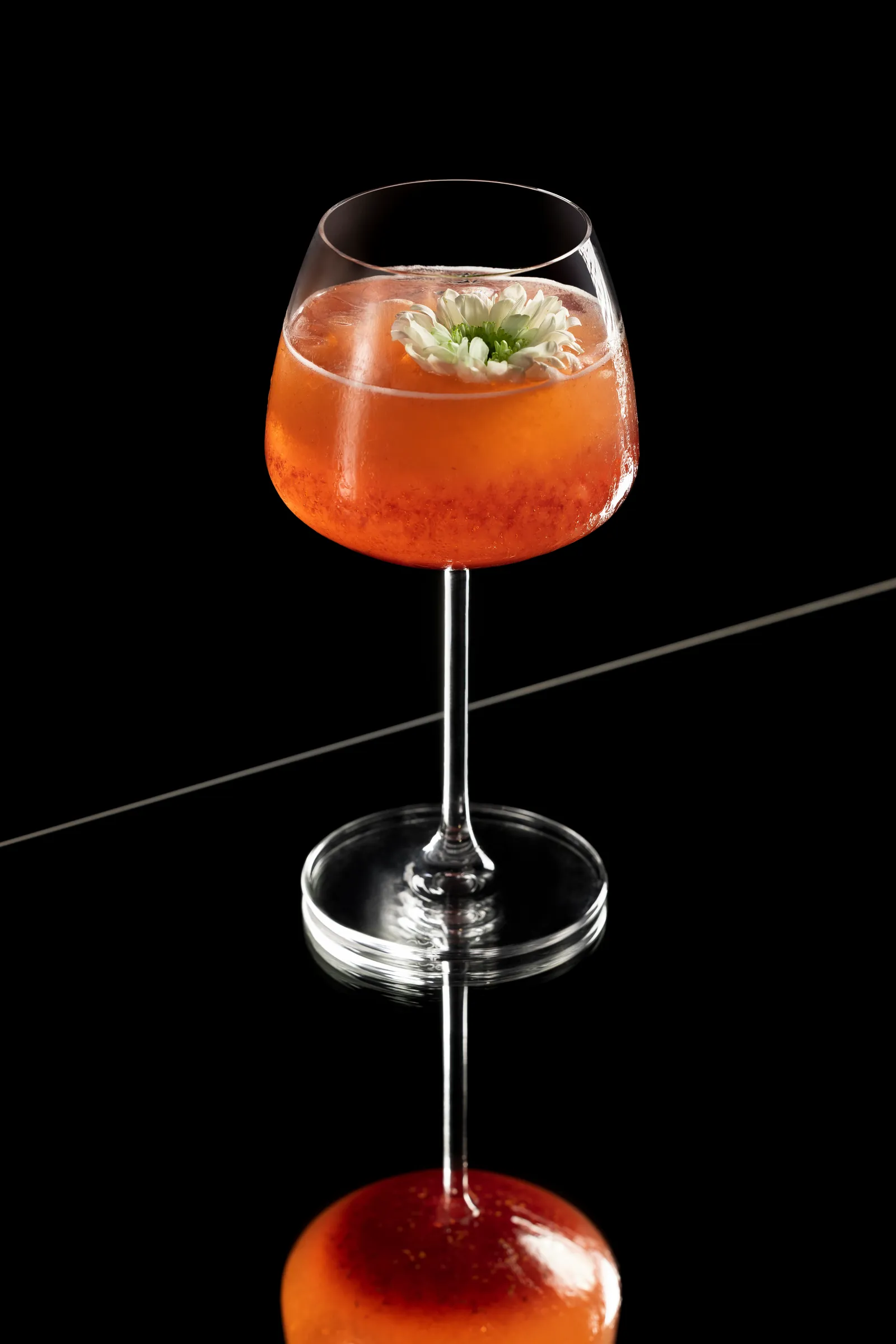 Garnished cocktail in a stemmed glass on a black reflective surface