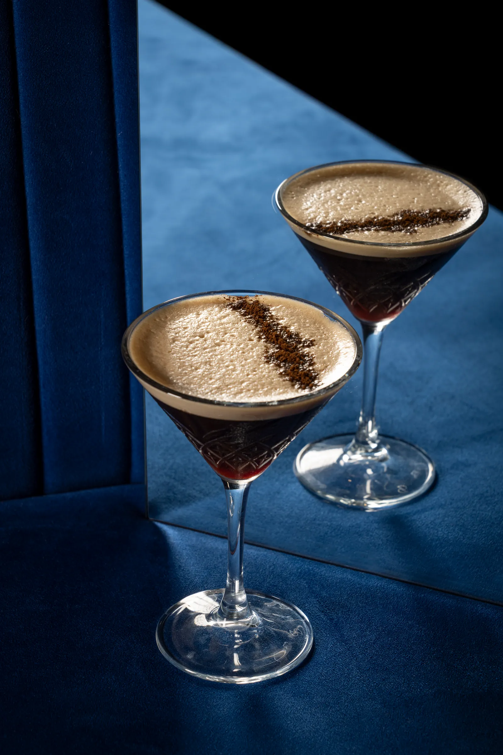 Two espresso martinis against a deep blue background