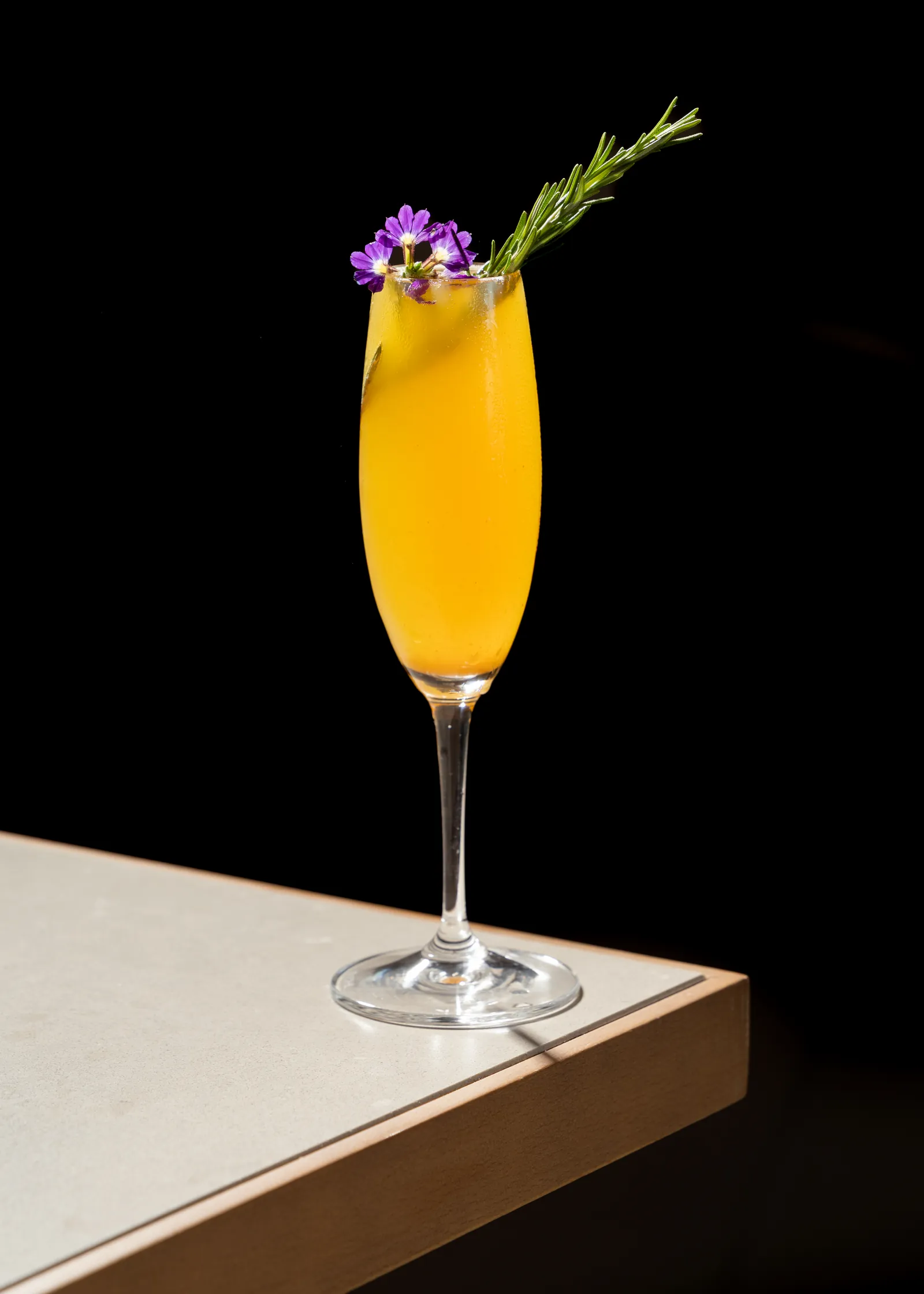 Orange cocktail in a champagne flute with a purple flower garnish