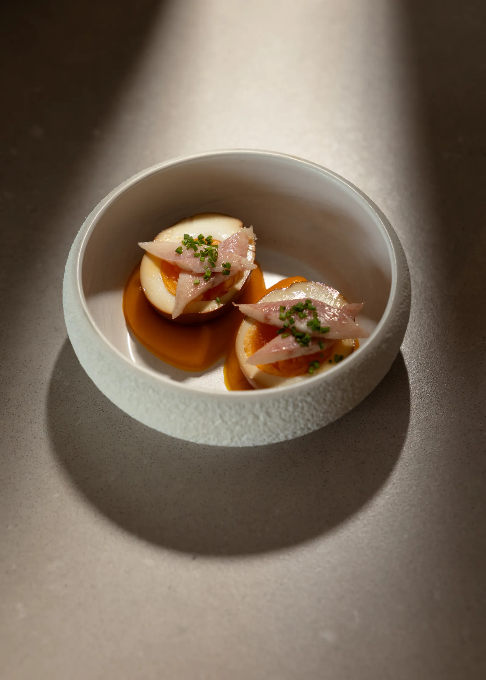 Seafood in a white bowl with sauce, lit by a diagonal shaft of light