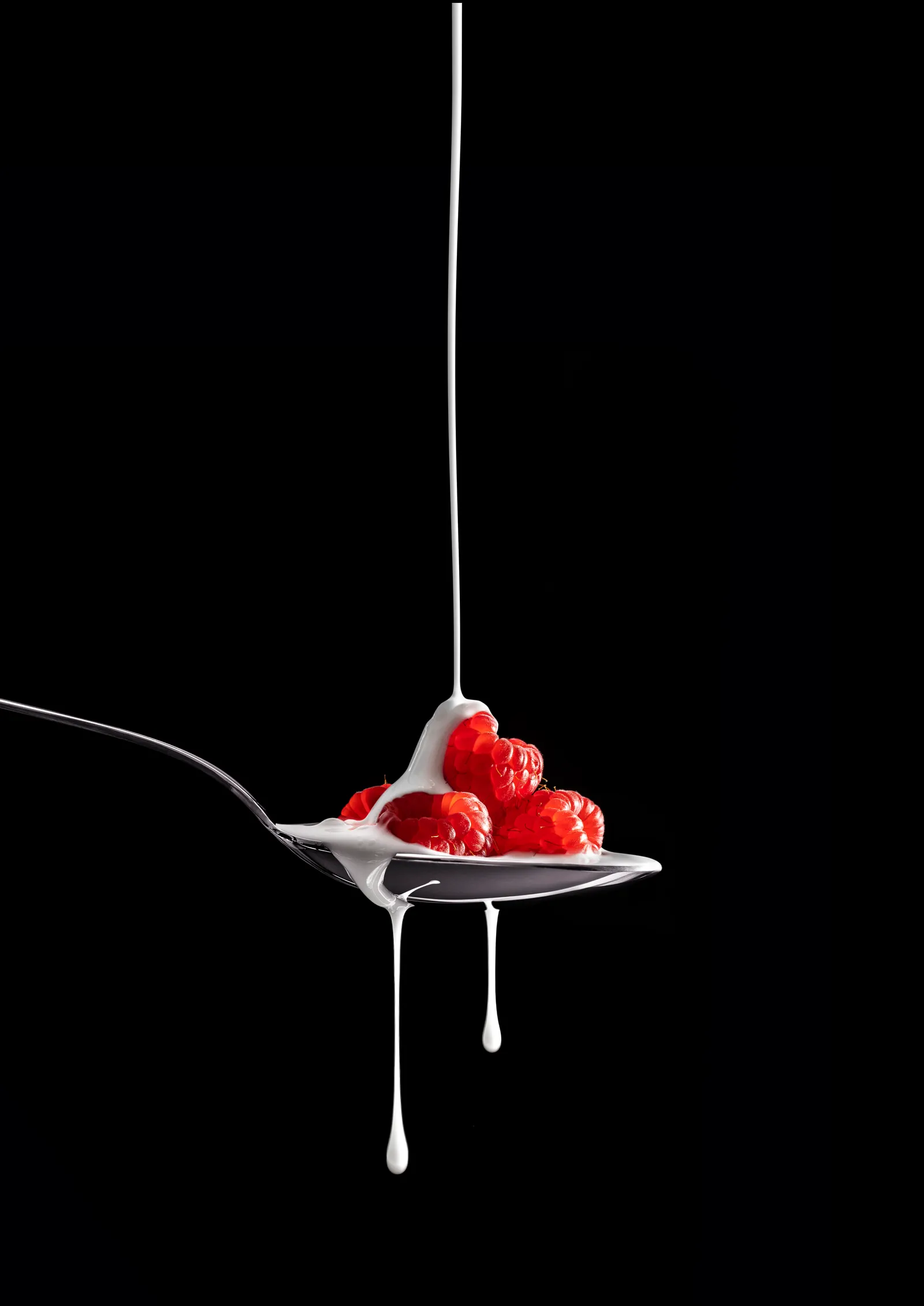 Raspberries on a spoon with a thin stream of syrup against black