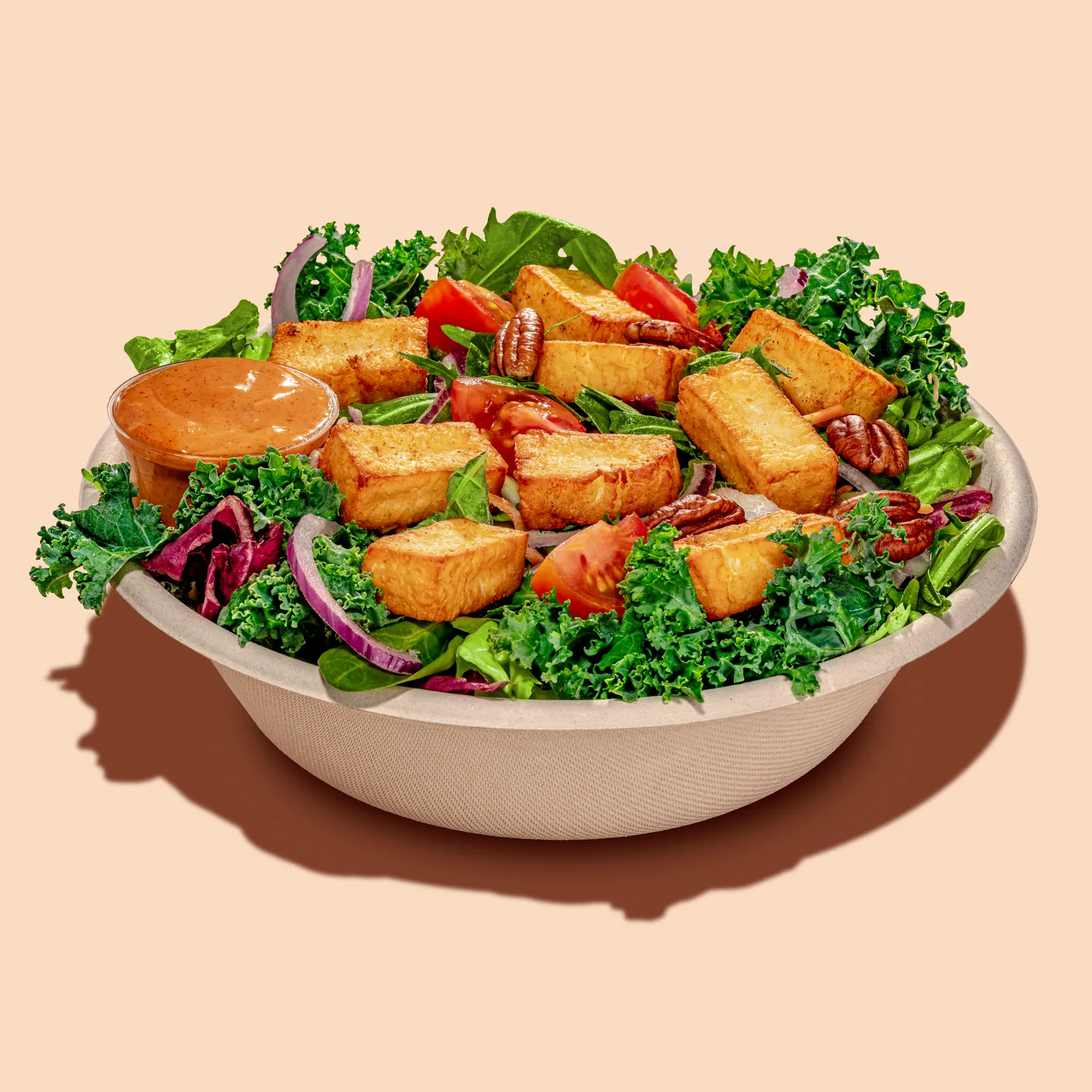 Kale salad with crispy tofu cubes and pecans in a bowl on a peach background, Chickoo