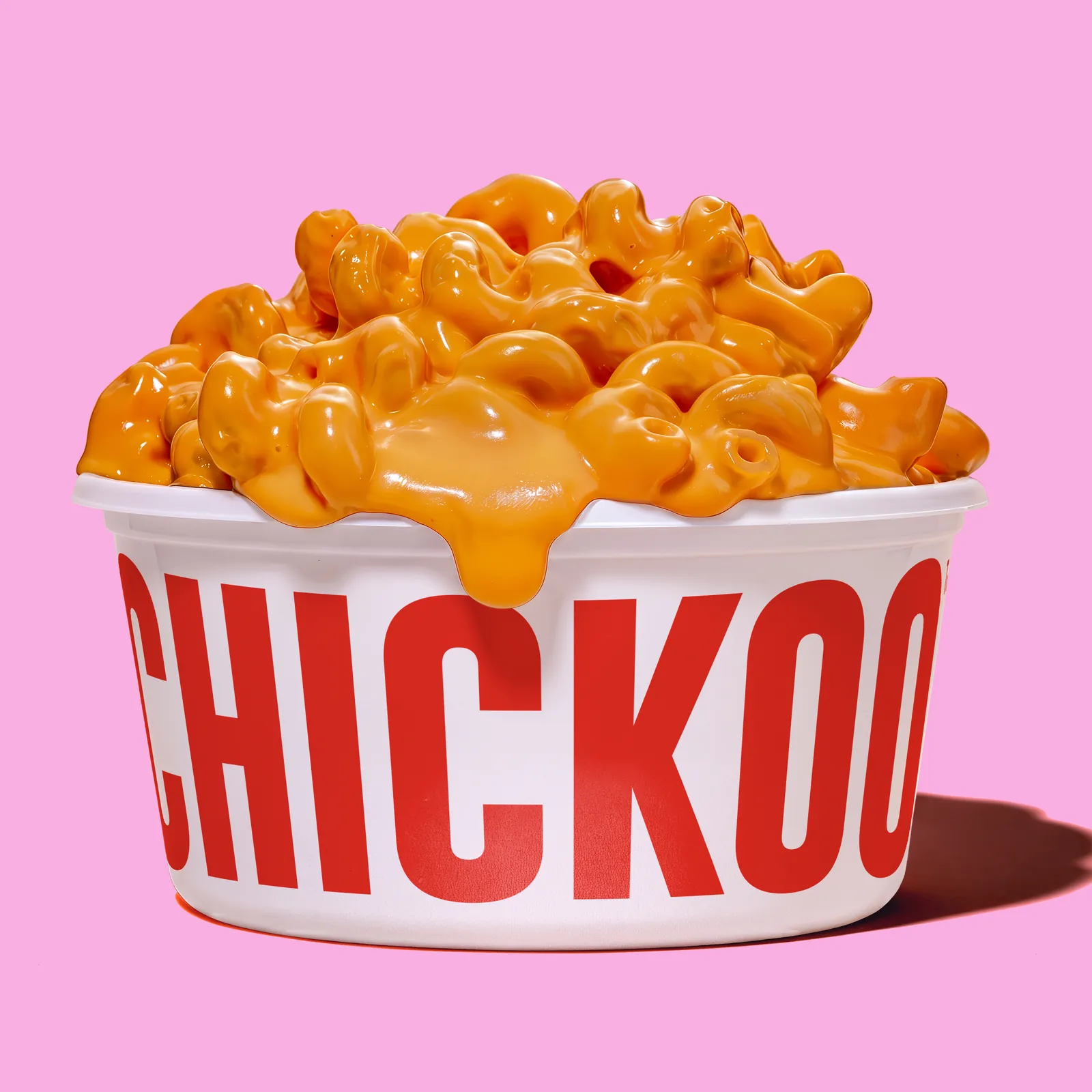 Mac and cheese spilling over a Chickoo tub on a pink background