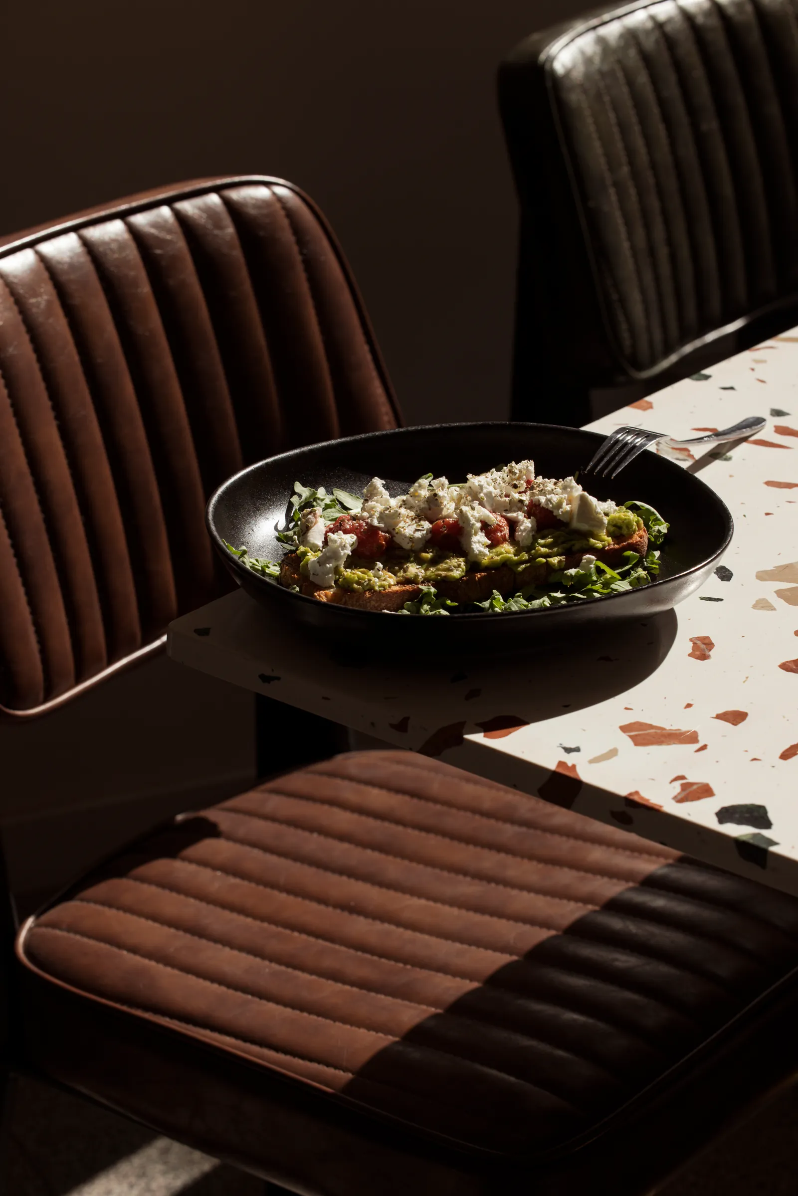 Salad in a dark bowl on a table beside leather chairs