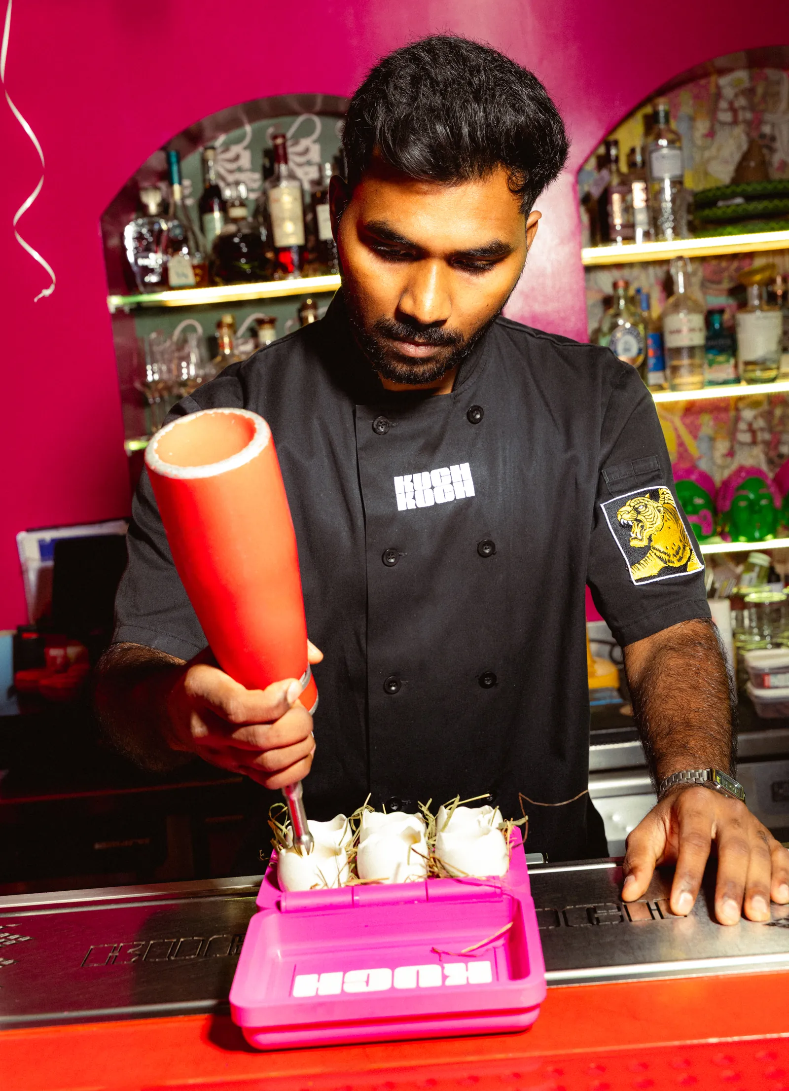 Bartender in a black shirt preparing drinks at a pink counter
