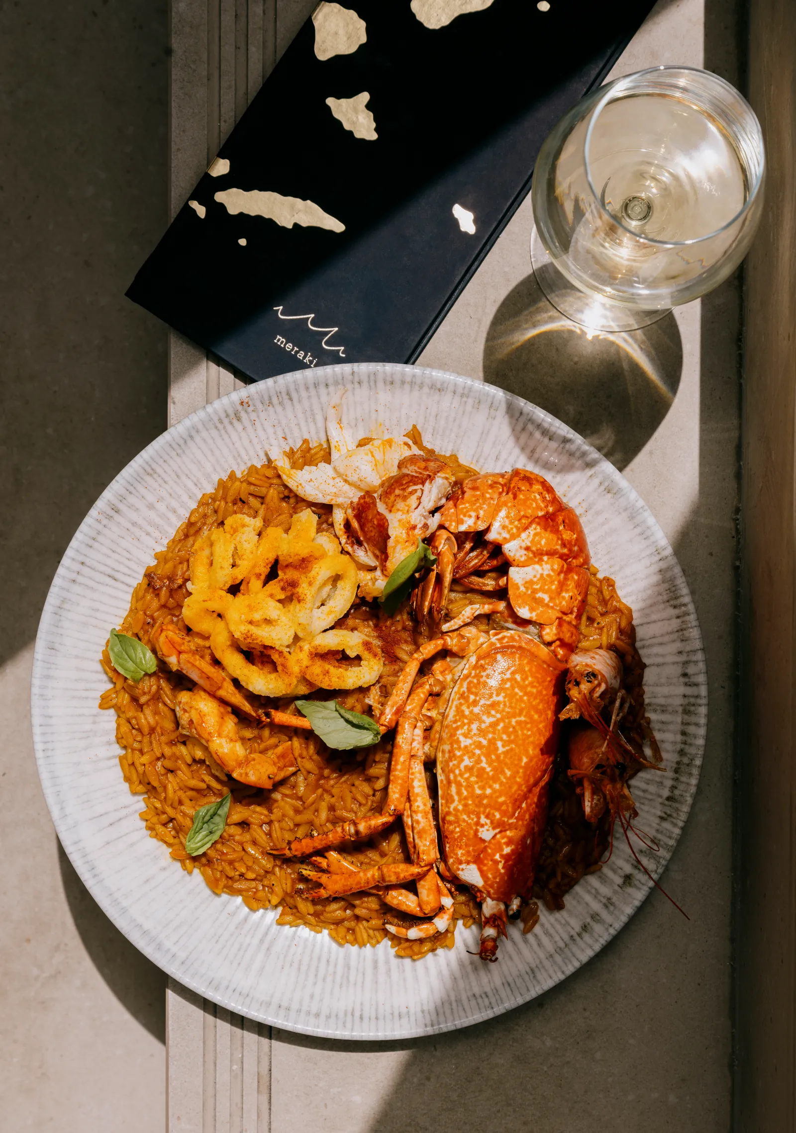 Lobster pasta on a plate beside a wine glass, seen from above