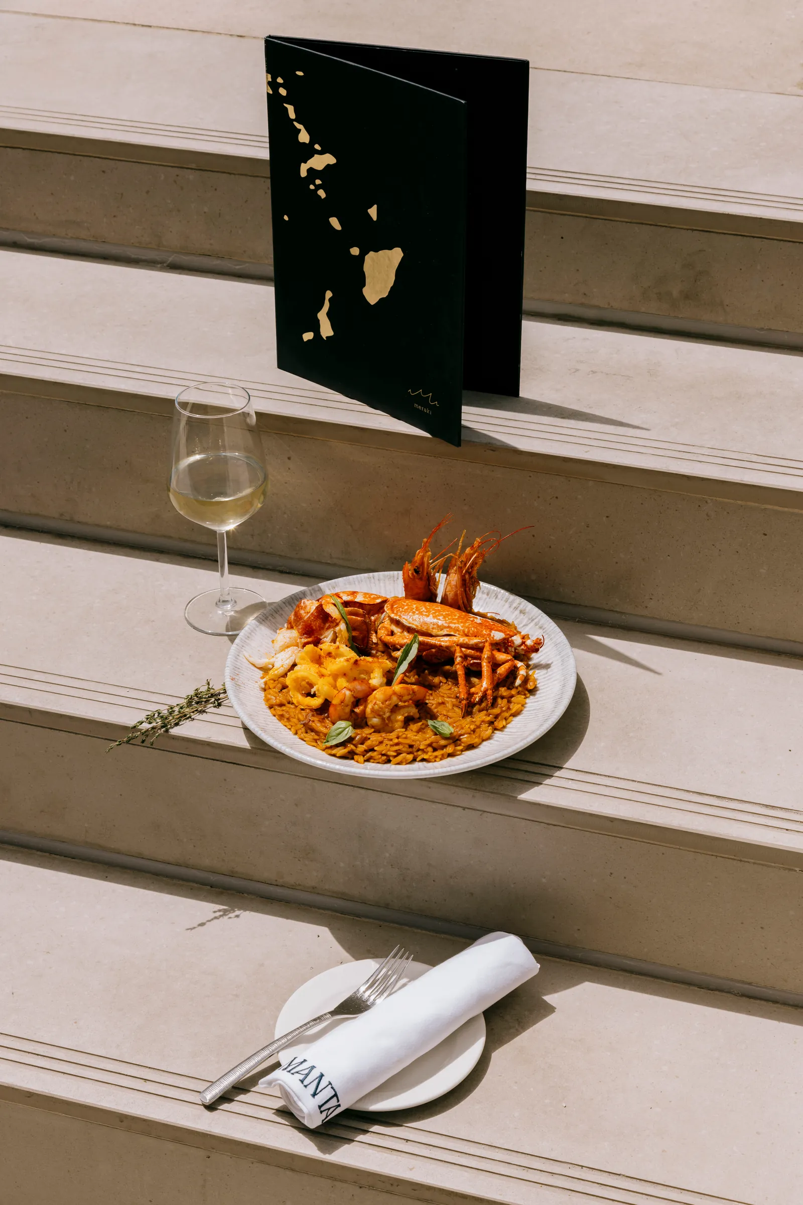 Pasta on a plate on stone steps, with a menu card and glass