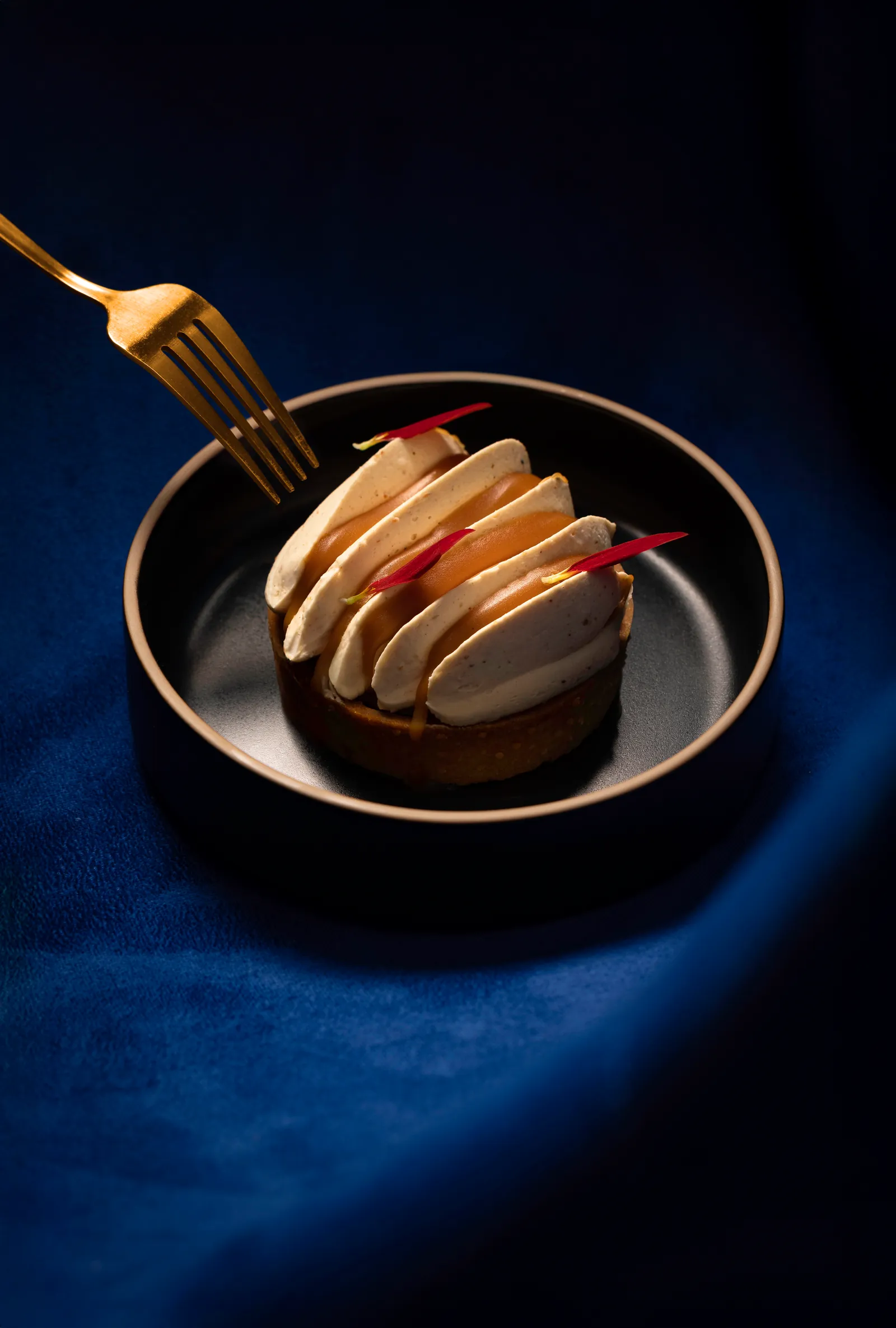 Fork lifting a piece of dessert from a dark bowl on blue