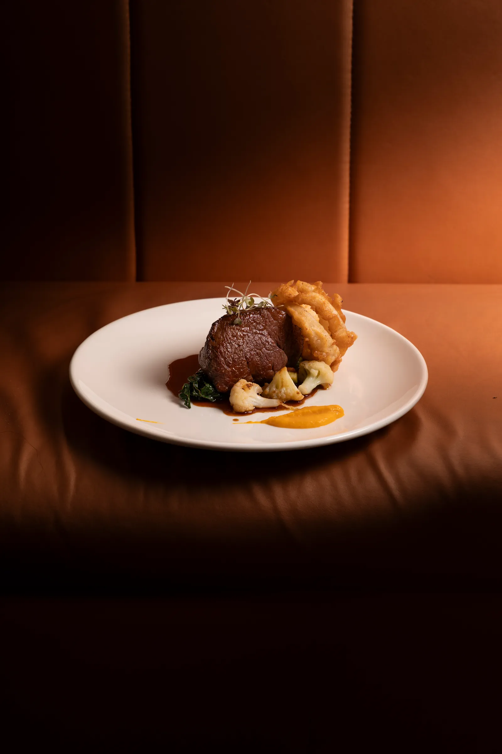Roast meat on a white plate in a leather booth