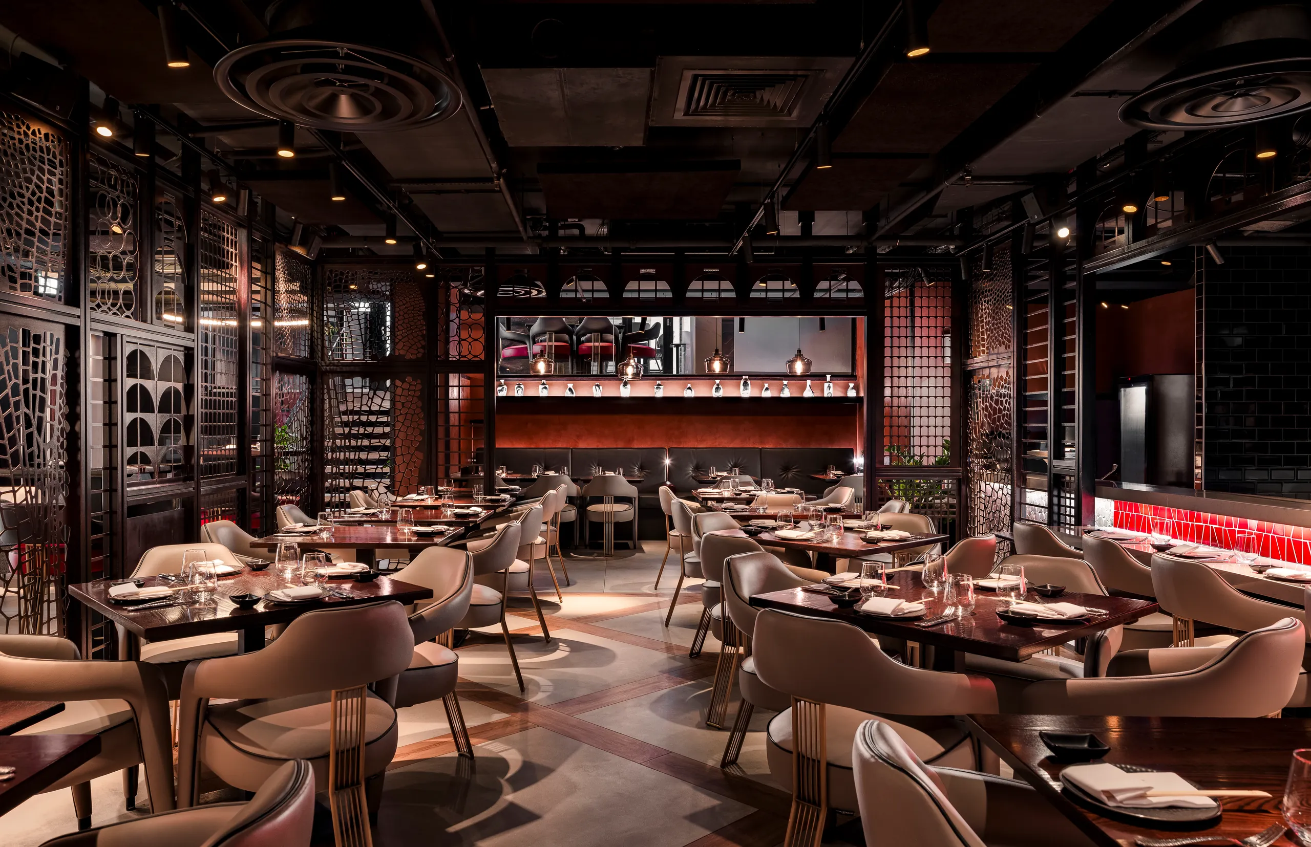 Large restaurant dining room with a dark ceiling, timber screens and a lit bar beyond