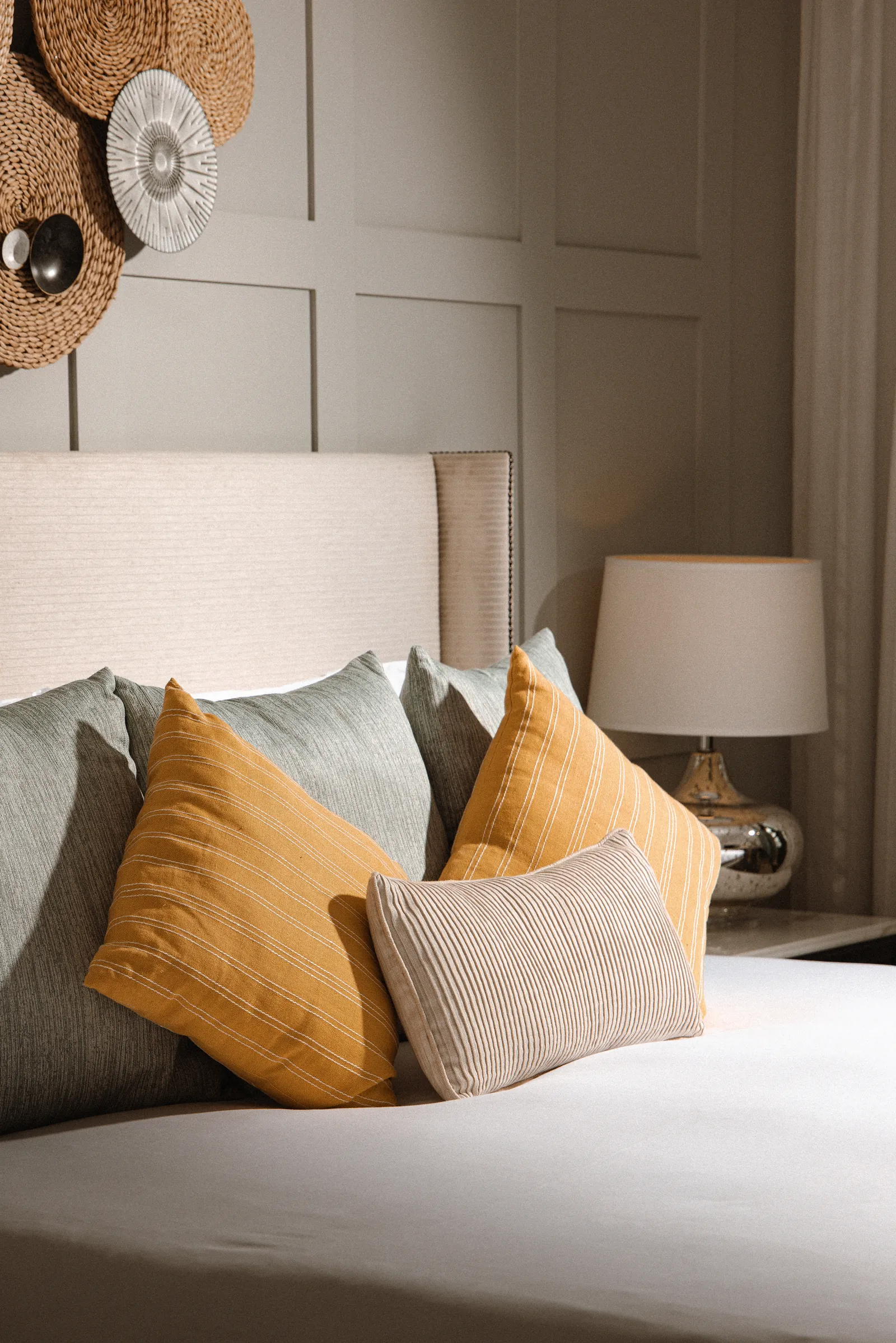 Bed with mustard and grey cushions and a bedside lamp in a Corinthia guest room