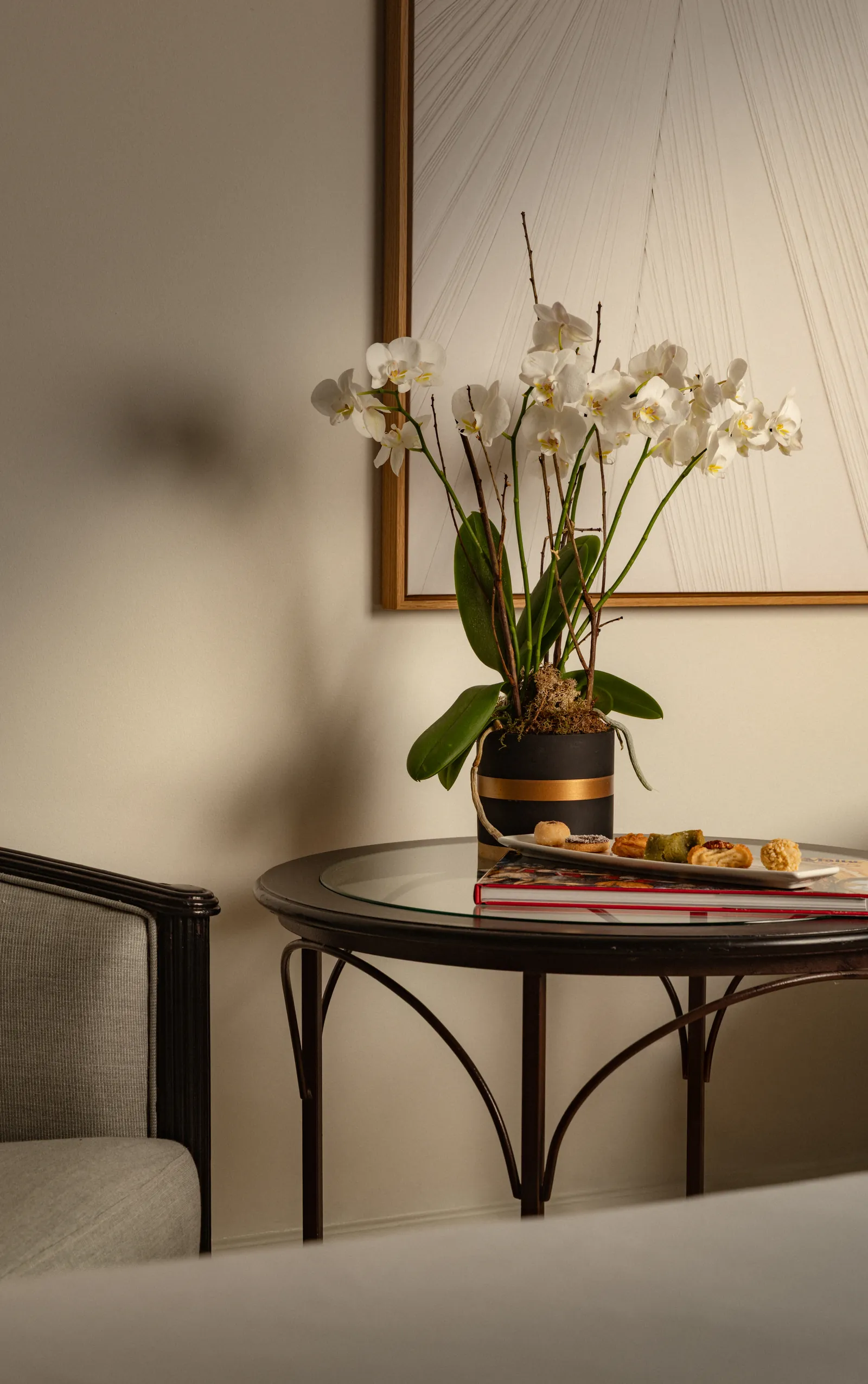 White orchids, books and a tray on a side table in a Corinthia St George's Bay guest room