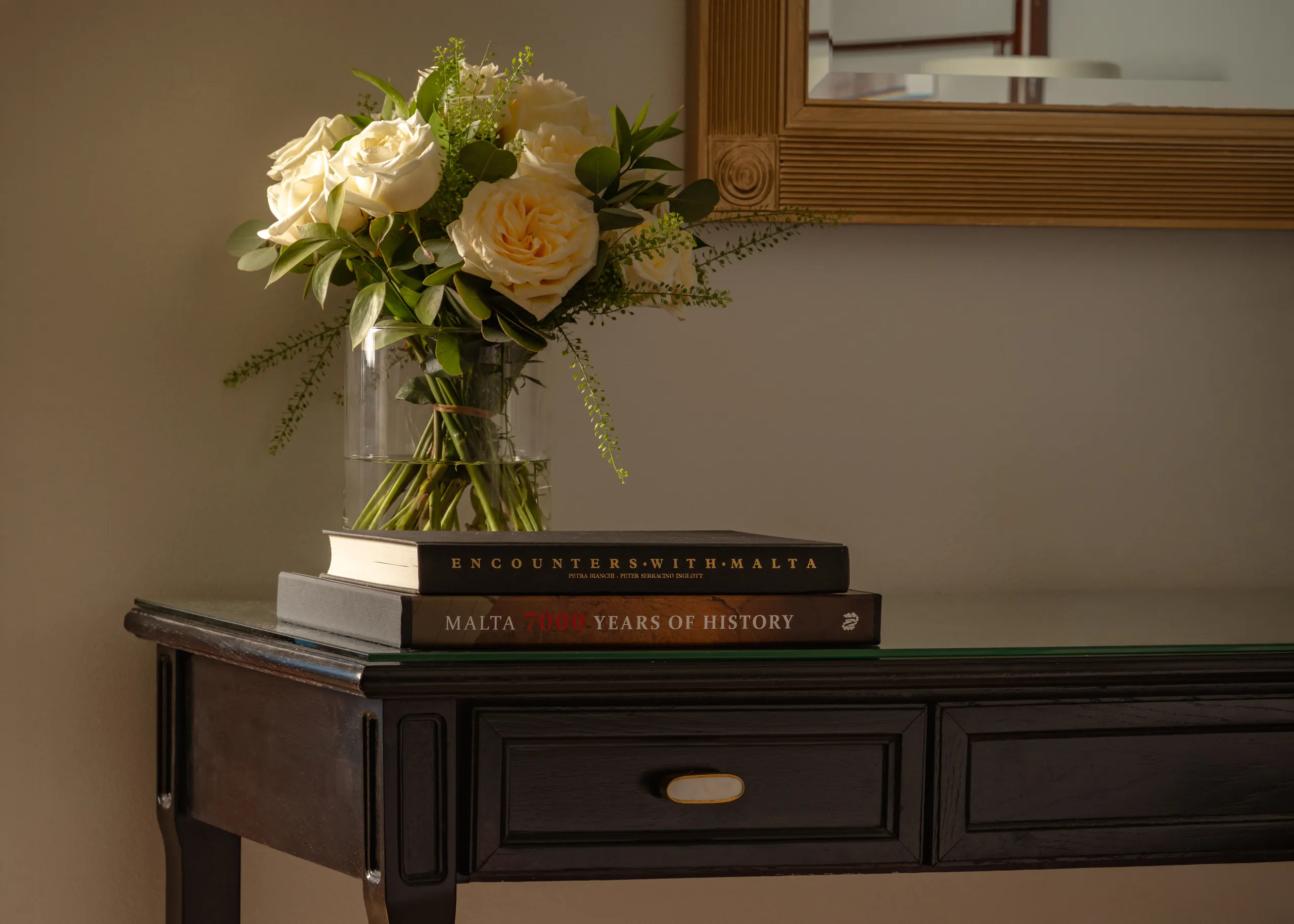Cream roses in a glass vase on a dark console table, Corinthia St George's Bay guest room