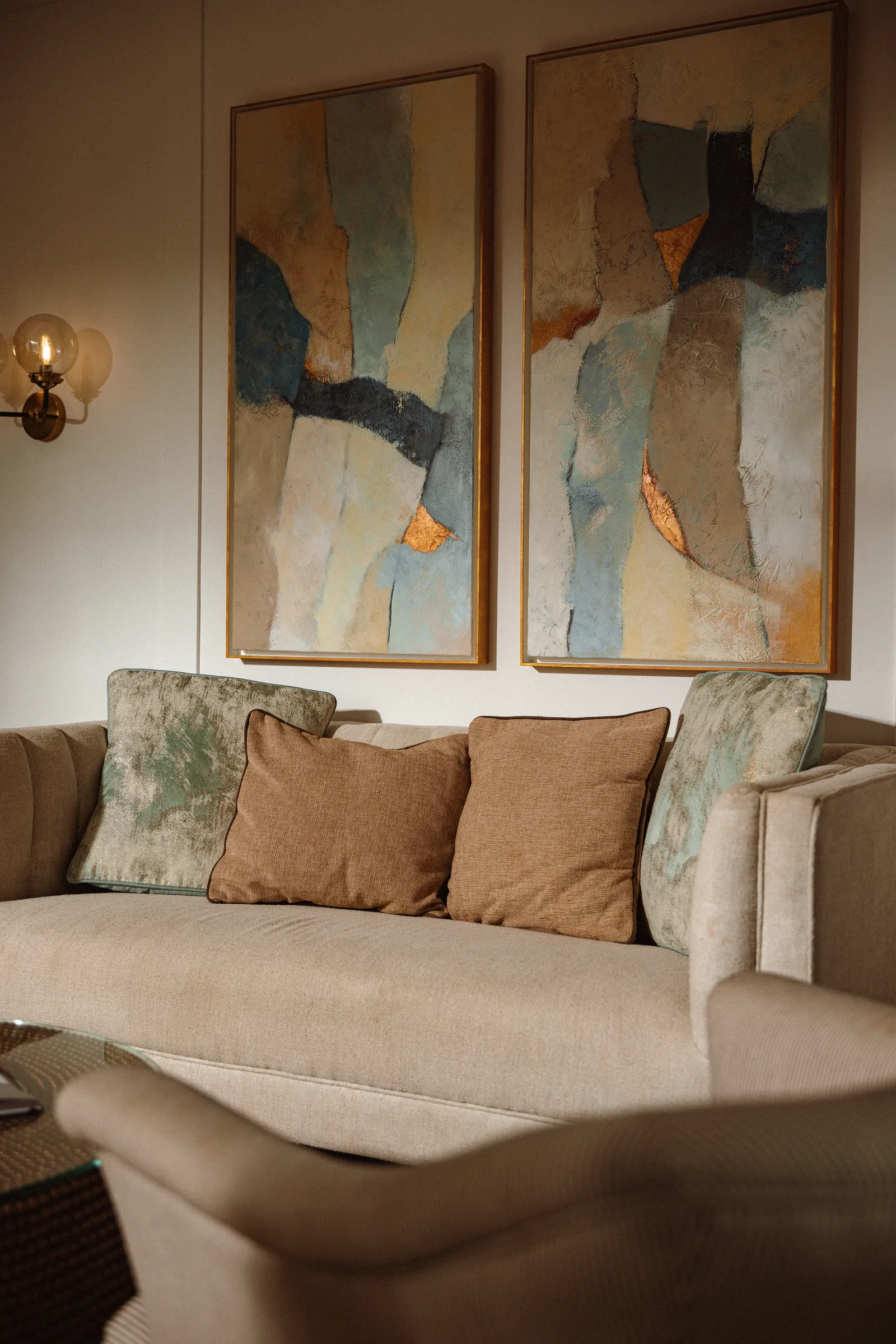Sofa with tan cushions beneath two abstract paintings