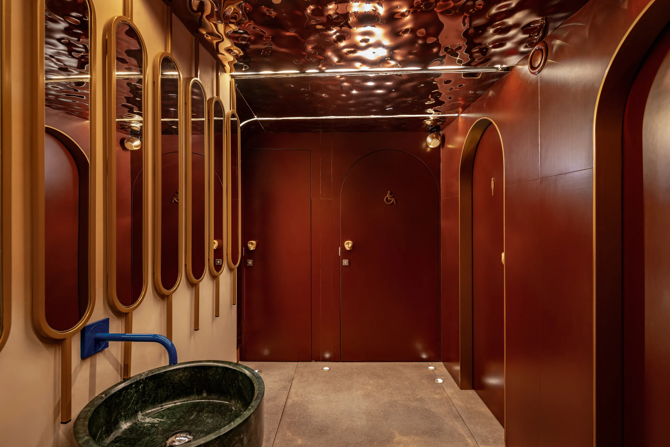 Washroom with arched mirrors, a green stone basin and a burgundy door