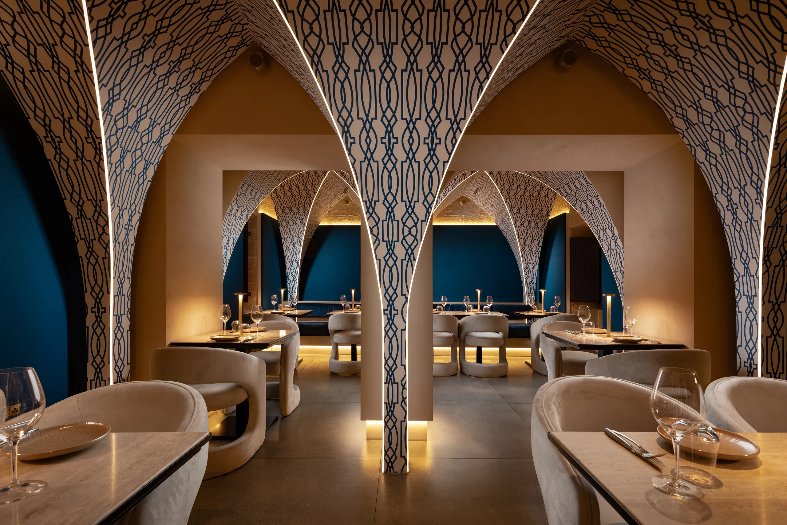 Restaurant with patterned arches over blue-lit booths and set tables