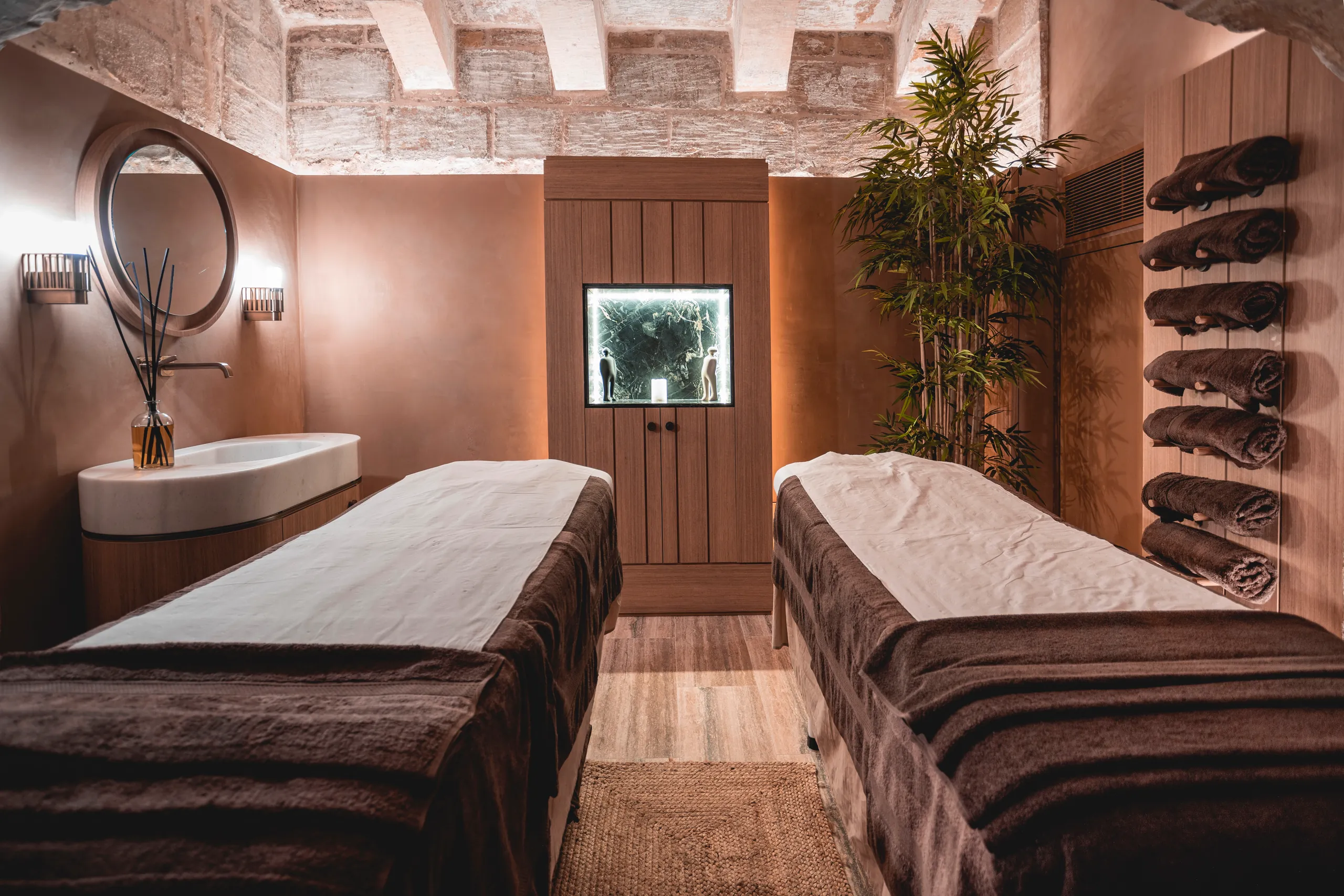 Spa treatment room with two massage beds, a basin and a rack of rolled towels