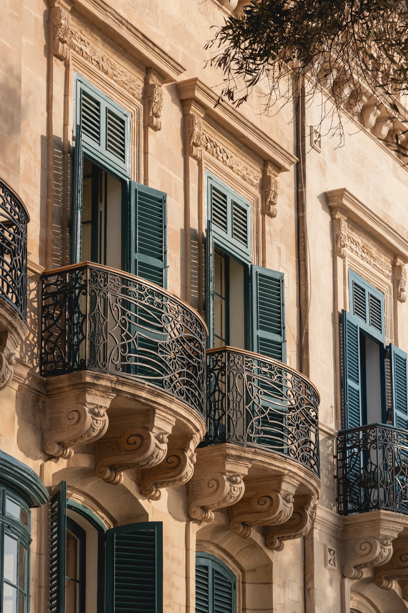 Ornate balconies with green shutters on a limestone façade