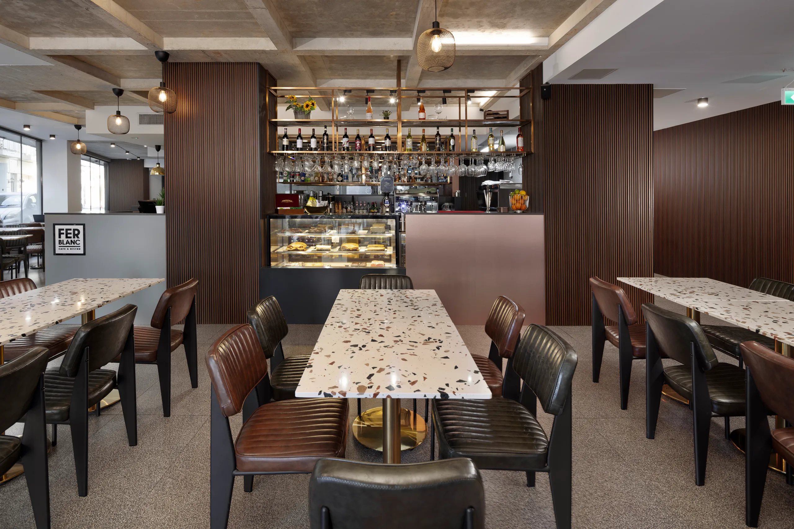 Restaurant with a long terrazzo-topped table, leather chairs and a bar with a cake display