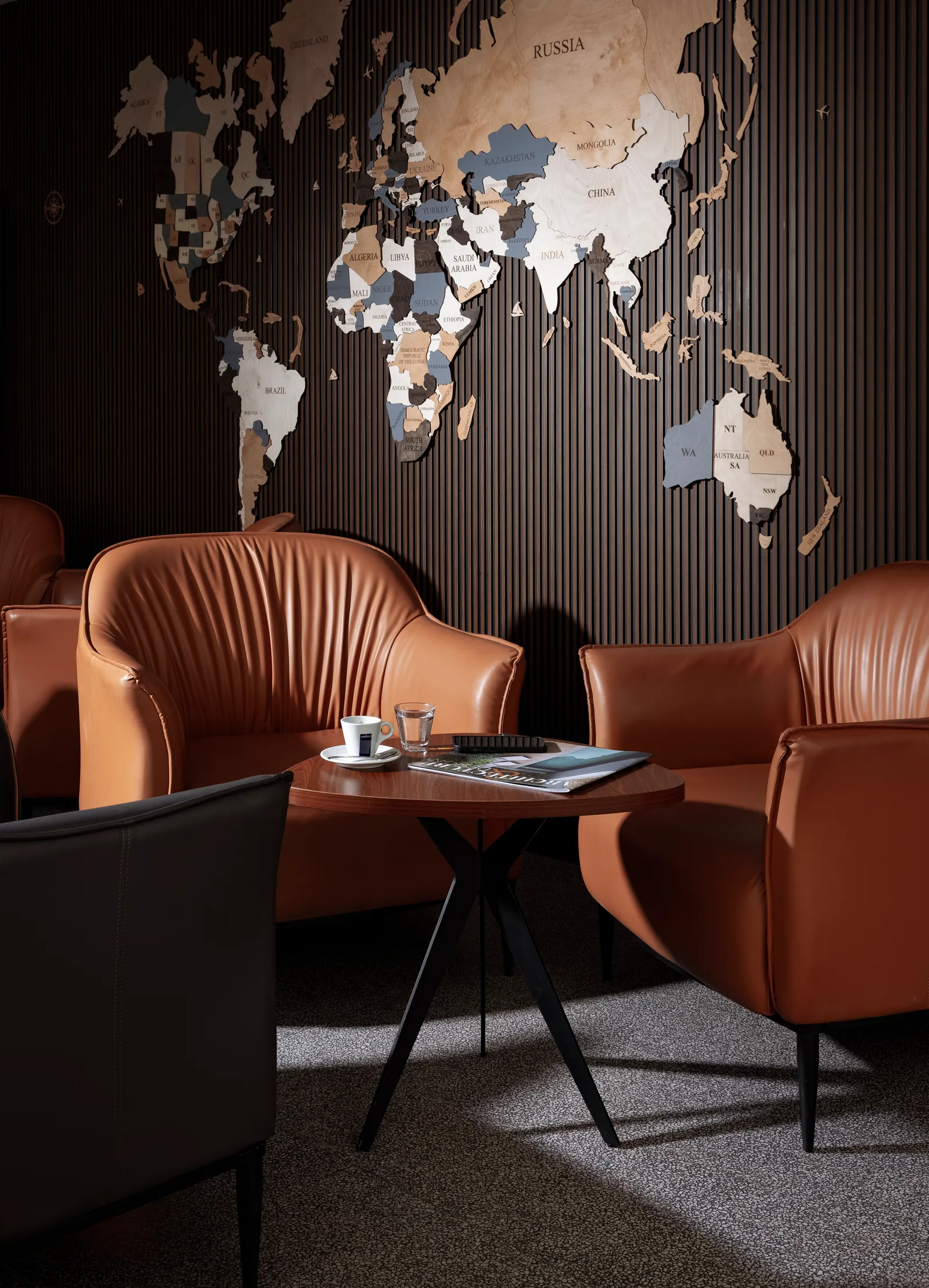 Tan leather armchairs and a side table beneath a wooden world-map wall