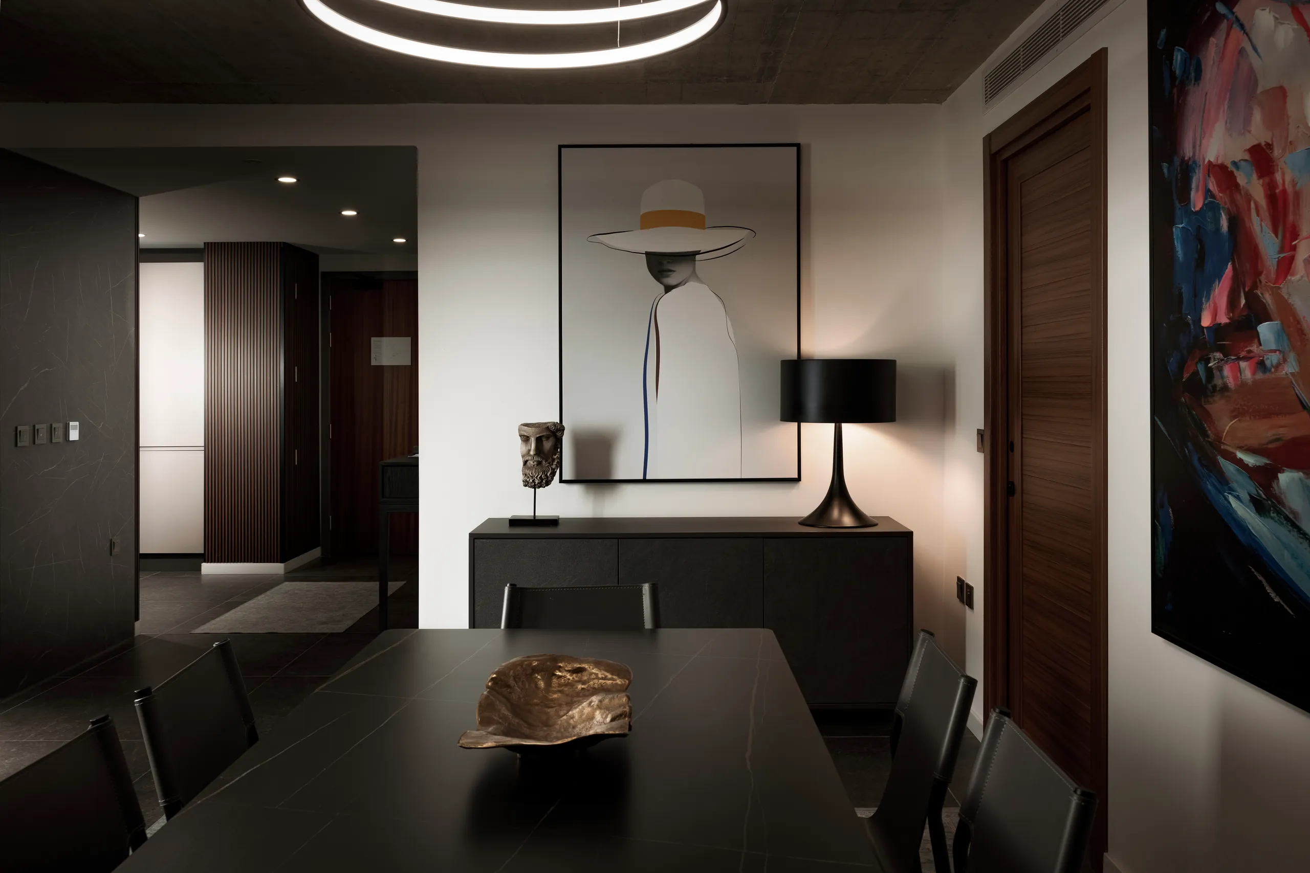 Dark dining table with a sideboard, lamp and framed artwork beneath a ring light