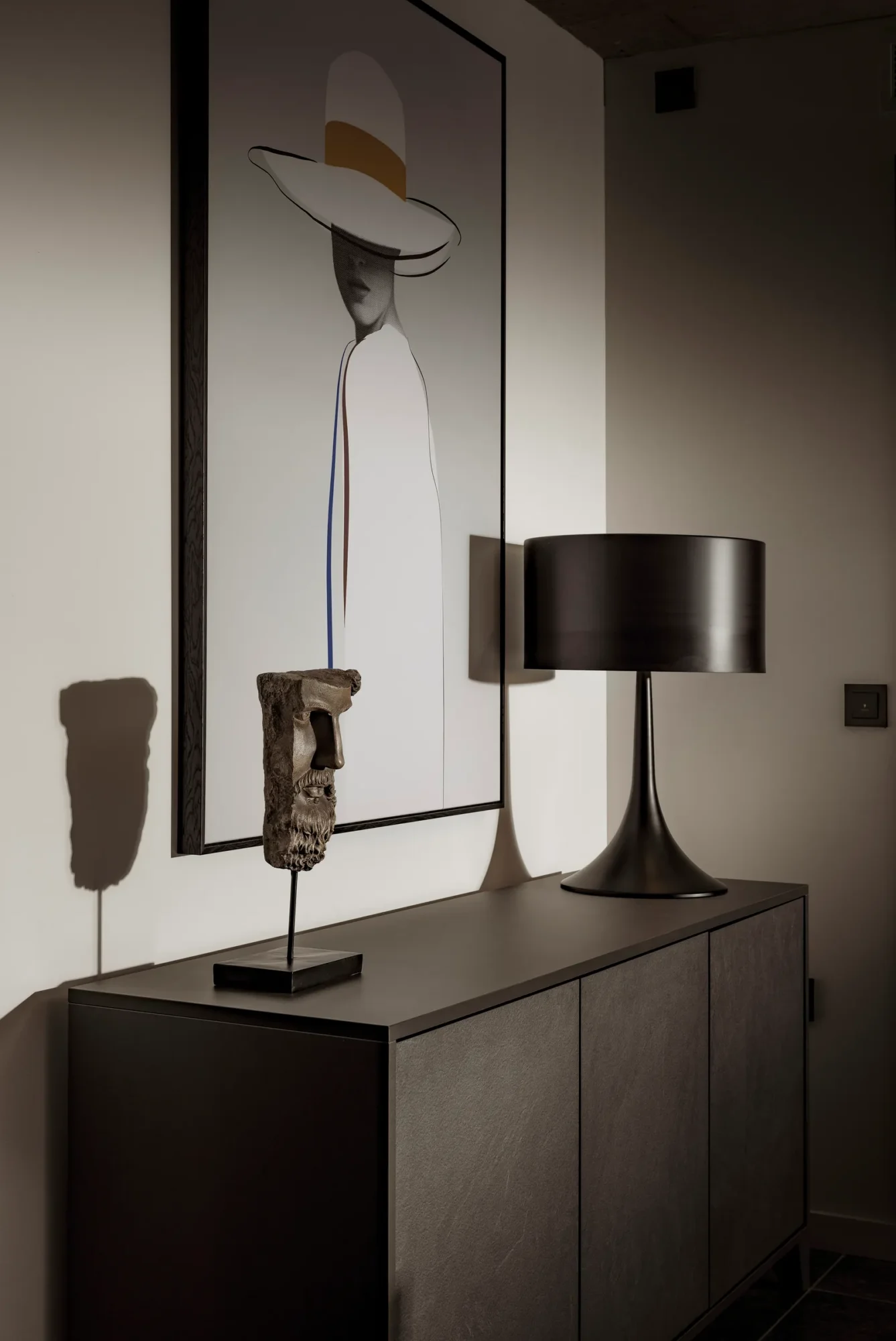 Black sideboard with a lamp and framed artwork of a woman in a hat