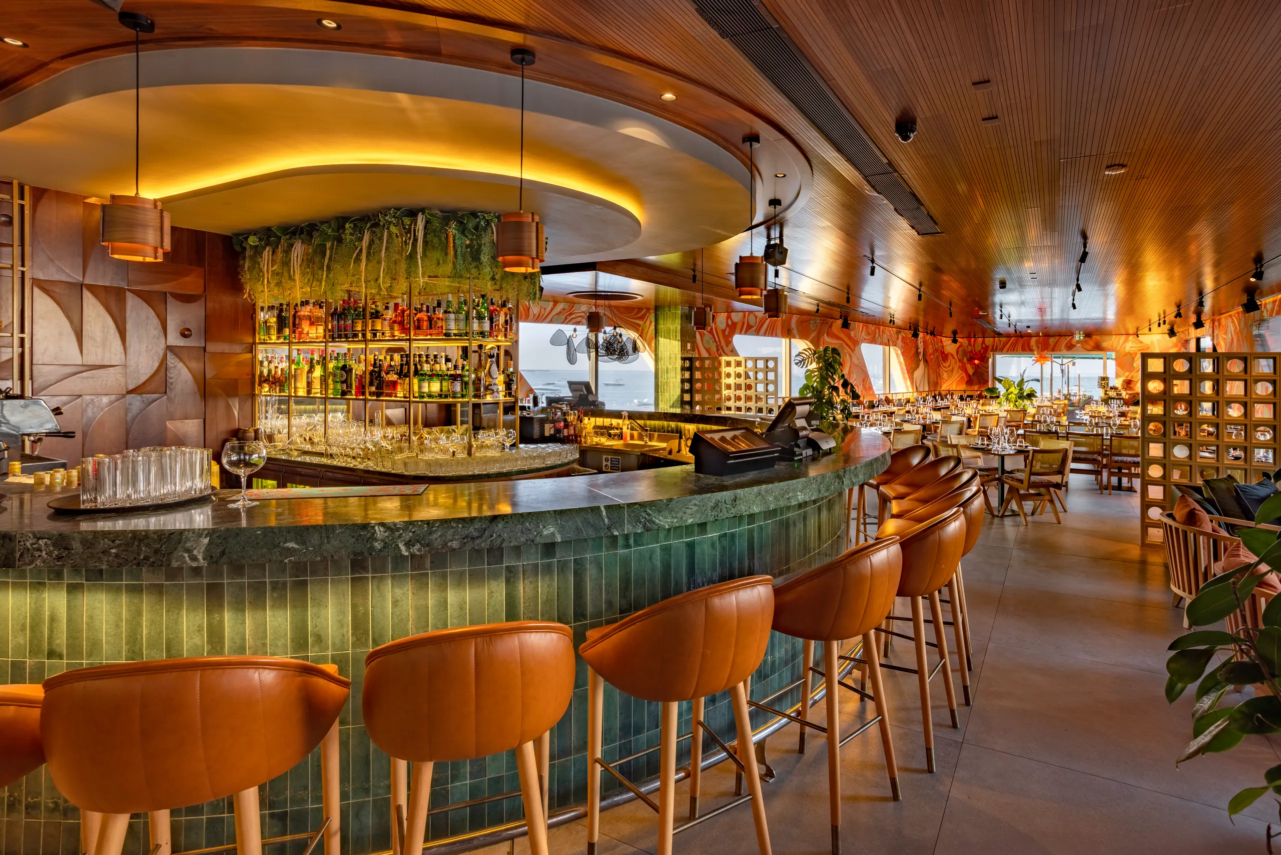 Round bar with orange stools, hanging plants and a lit glass backdrop