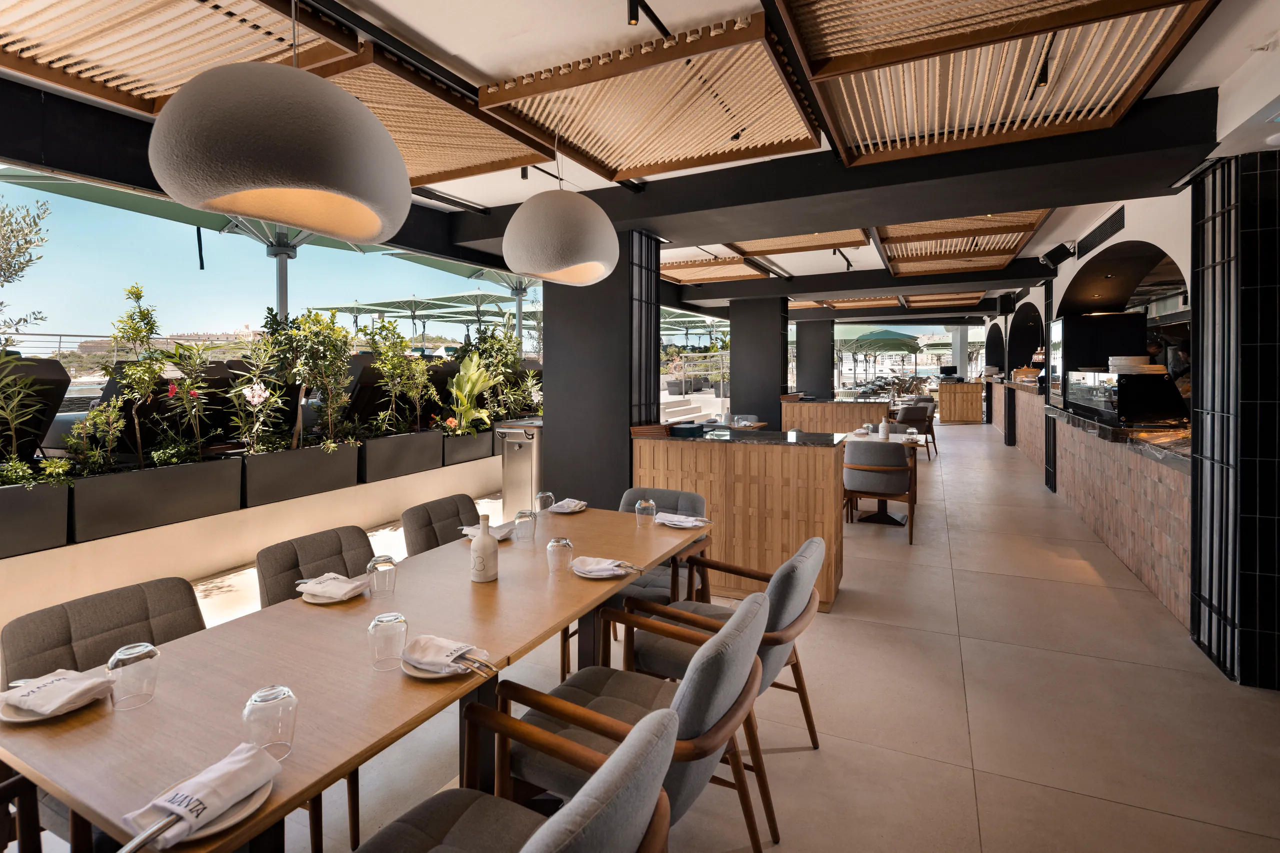 Open-air restaurant with a long table, pendant lights and plants along the terrace