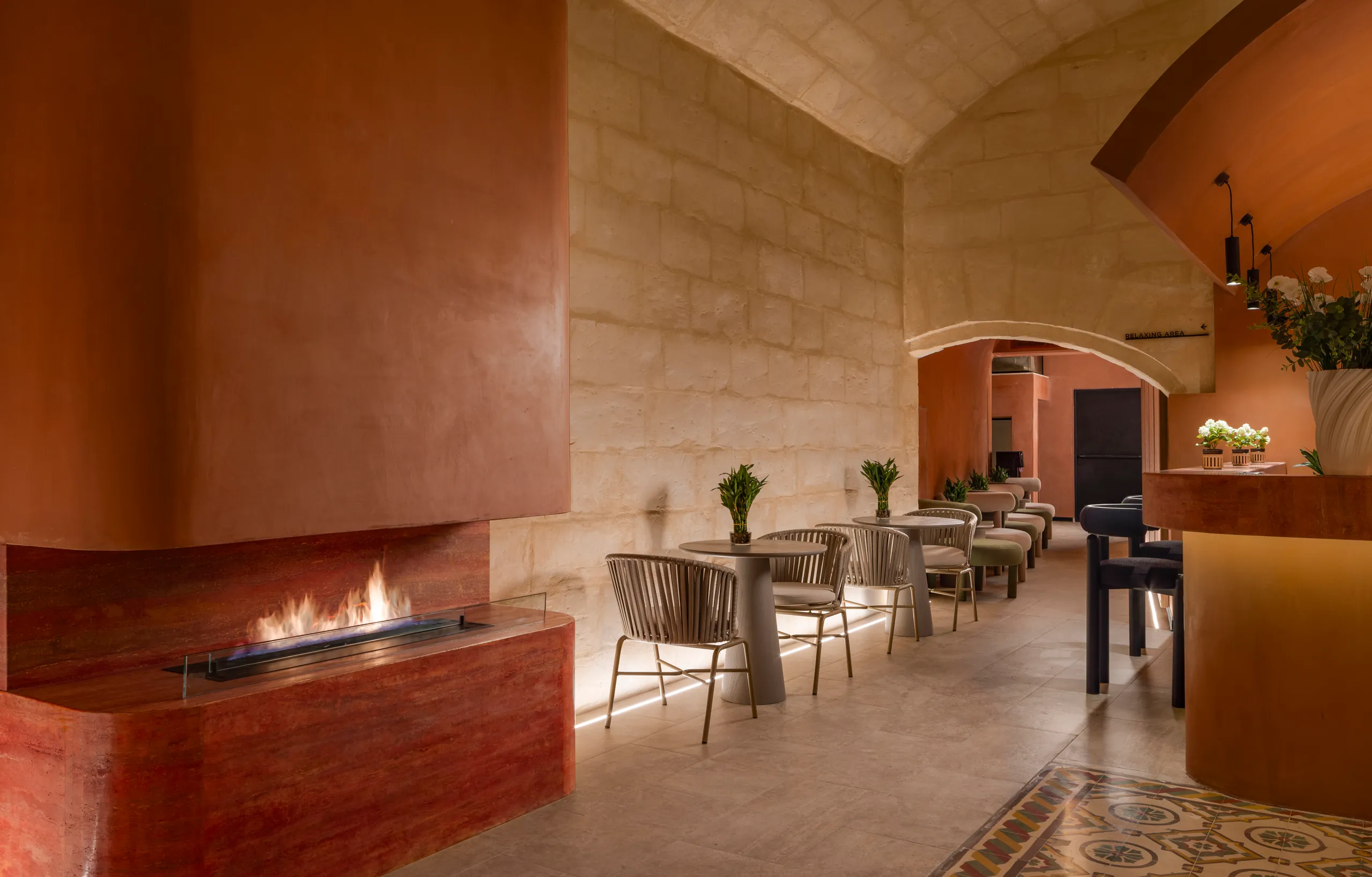 Terracotta fireplace in a vaulted limestone spa lounge with café tables beyond