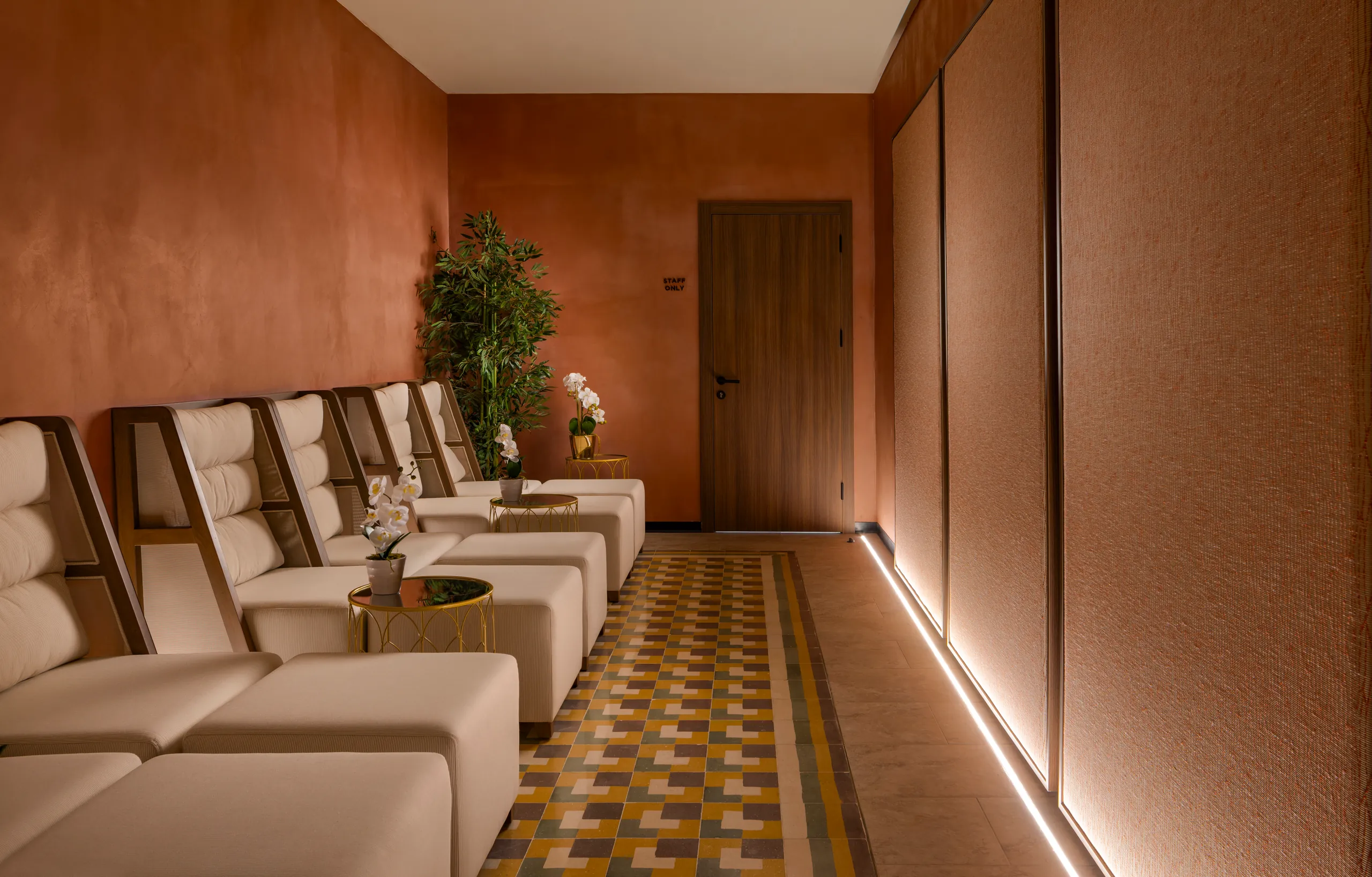 Row of cream loungers in a spa corridor with patterned floor tiles and terracotta walls
