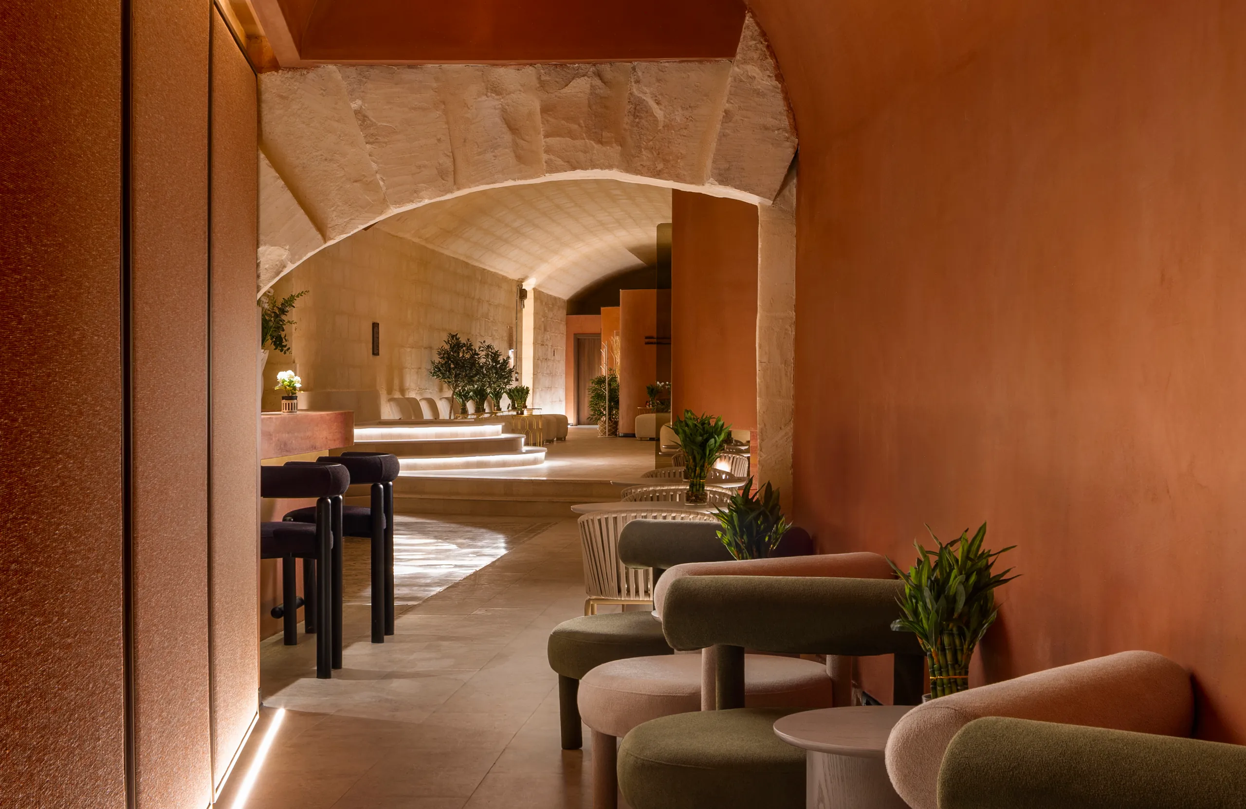 Terracotta-walled spa lounge seen through an arch, with green armchairs and small tables