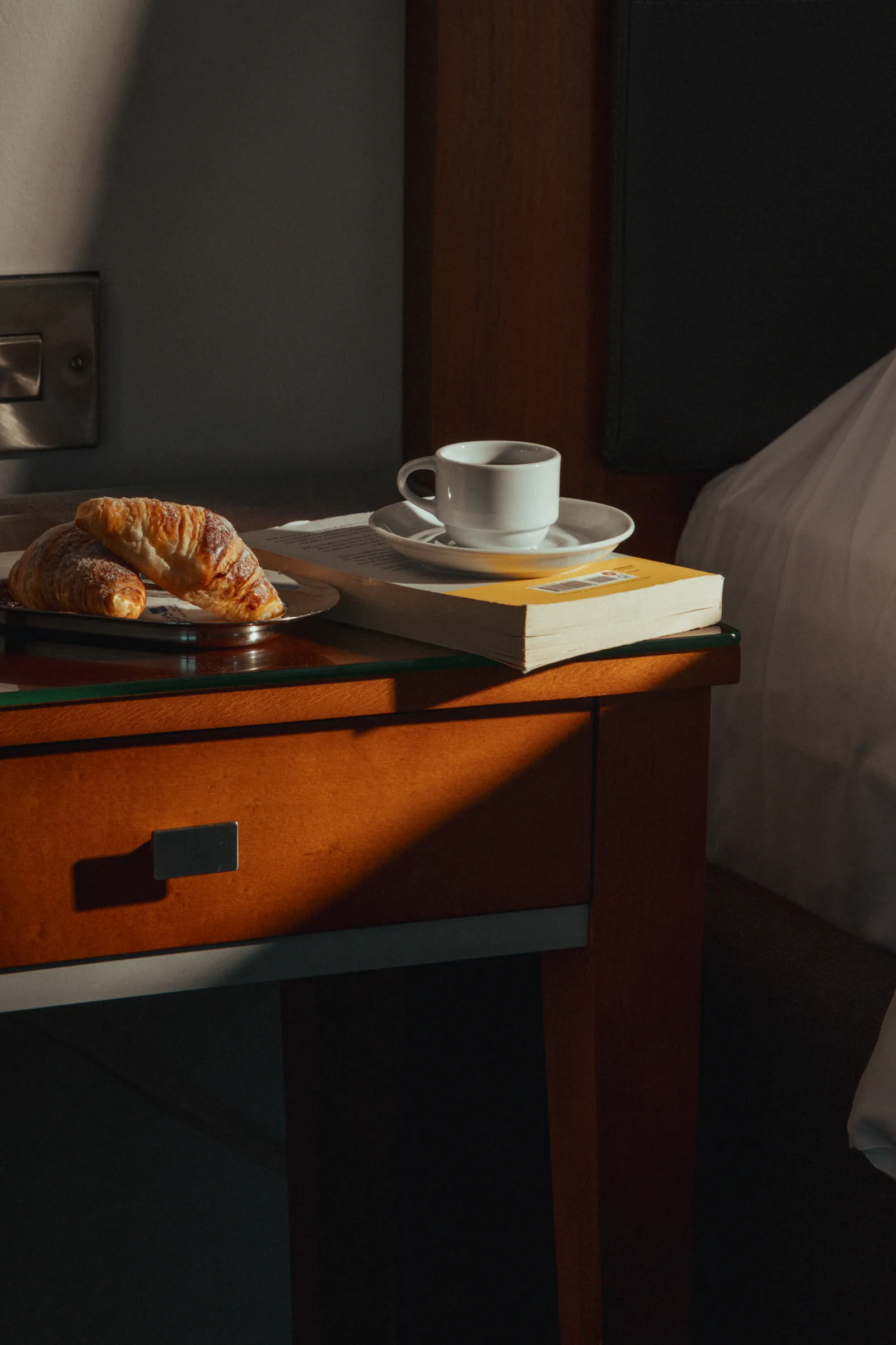 Cup of coffee and a pastry on a wooden bedside shelf