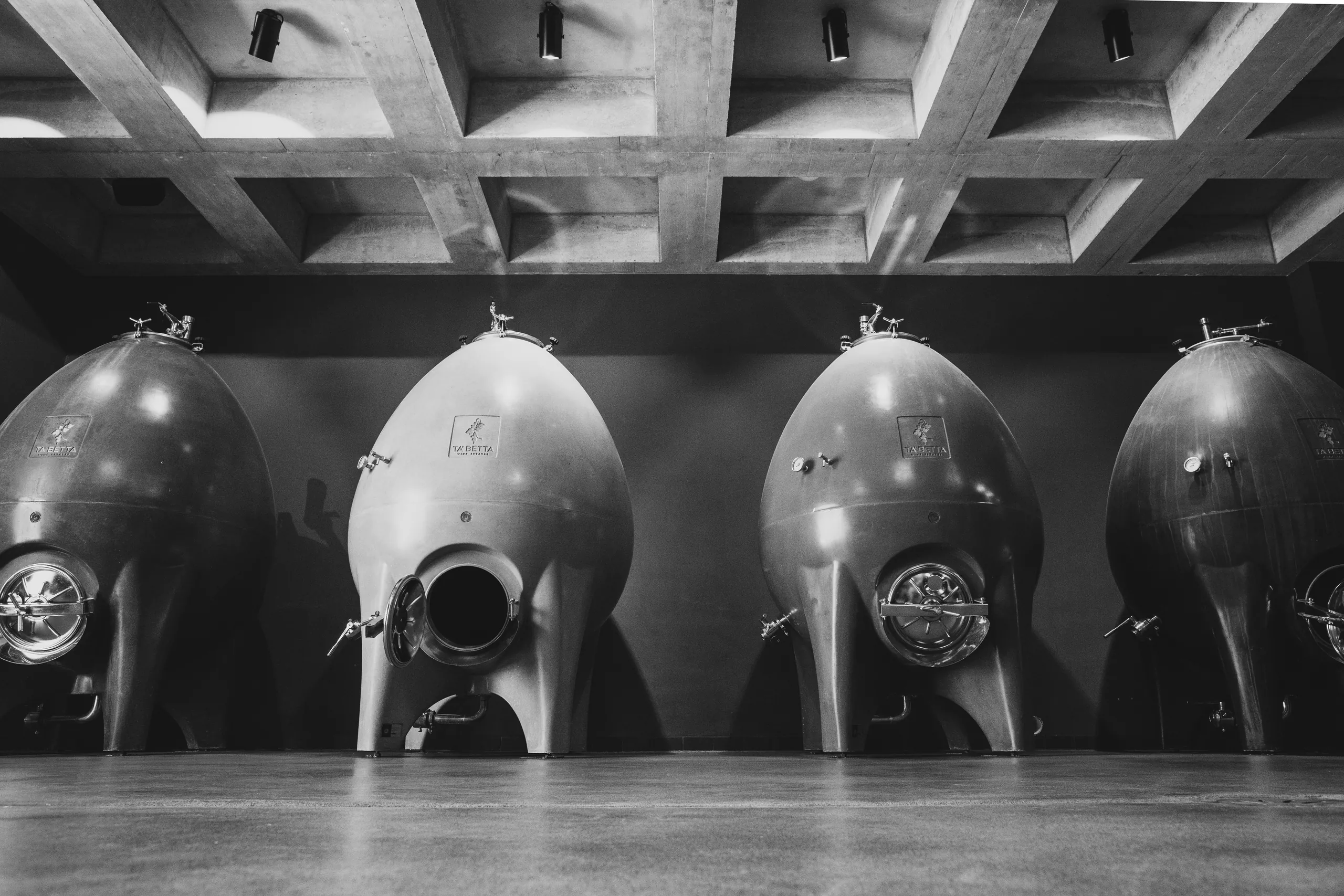 Black-and-white image of four rounded metal tanks beneath a coffered concrete ceiling
