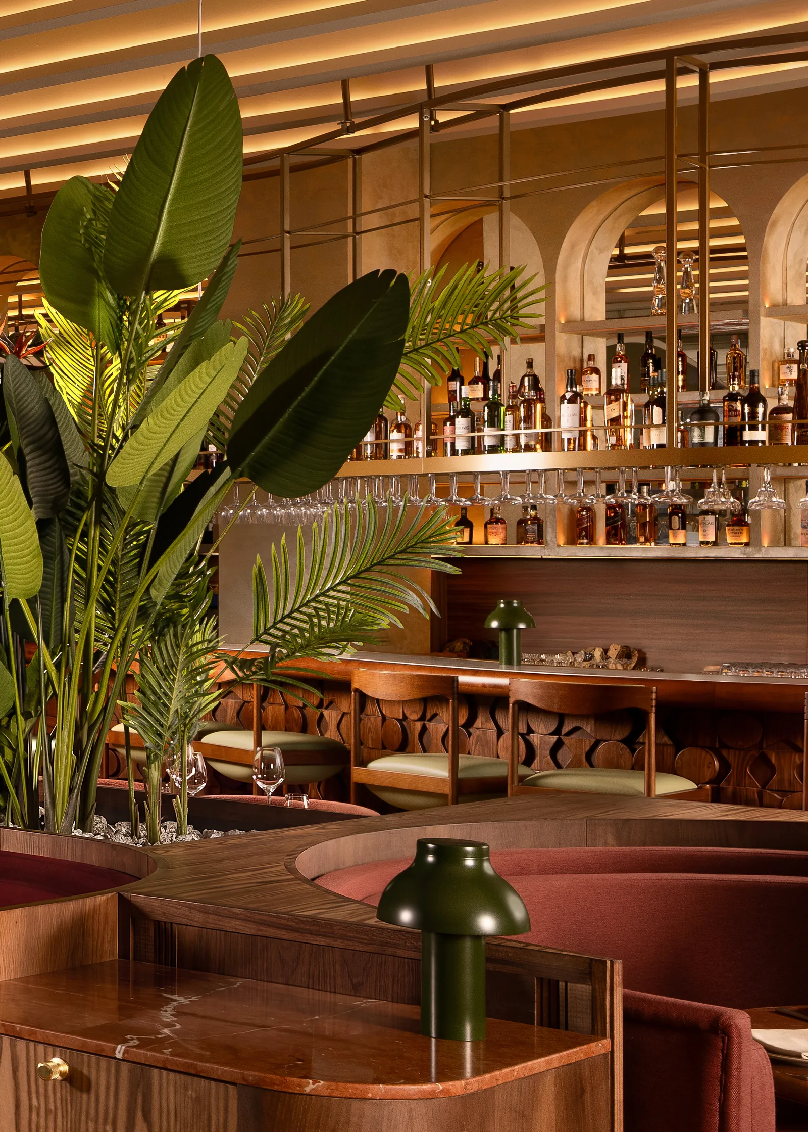 Curved booth and tropical plants in the lounge at Tanvi, with the bar shelves behind