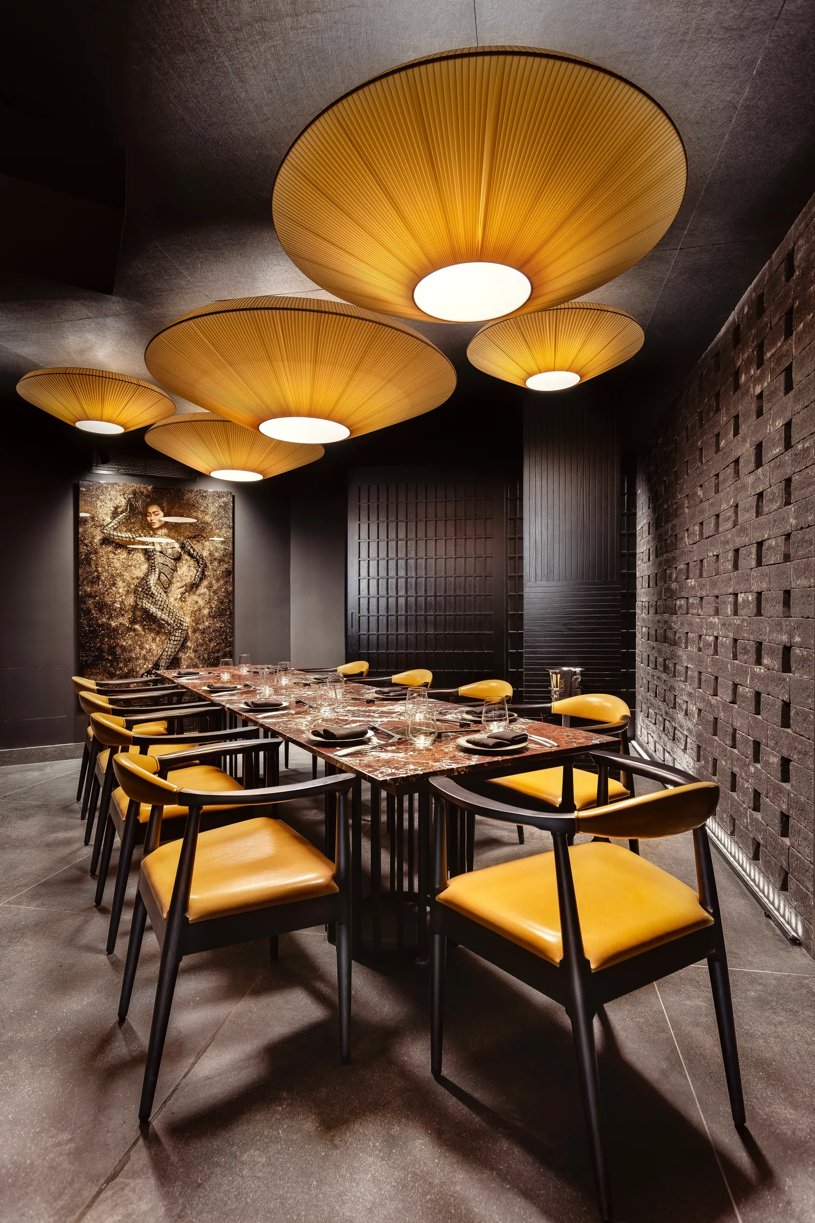 Tables with mustard-yellow chairs under woven pendant lamps at Tora