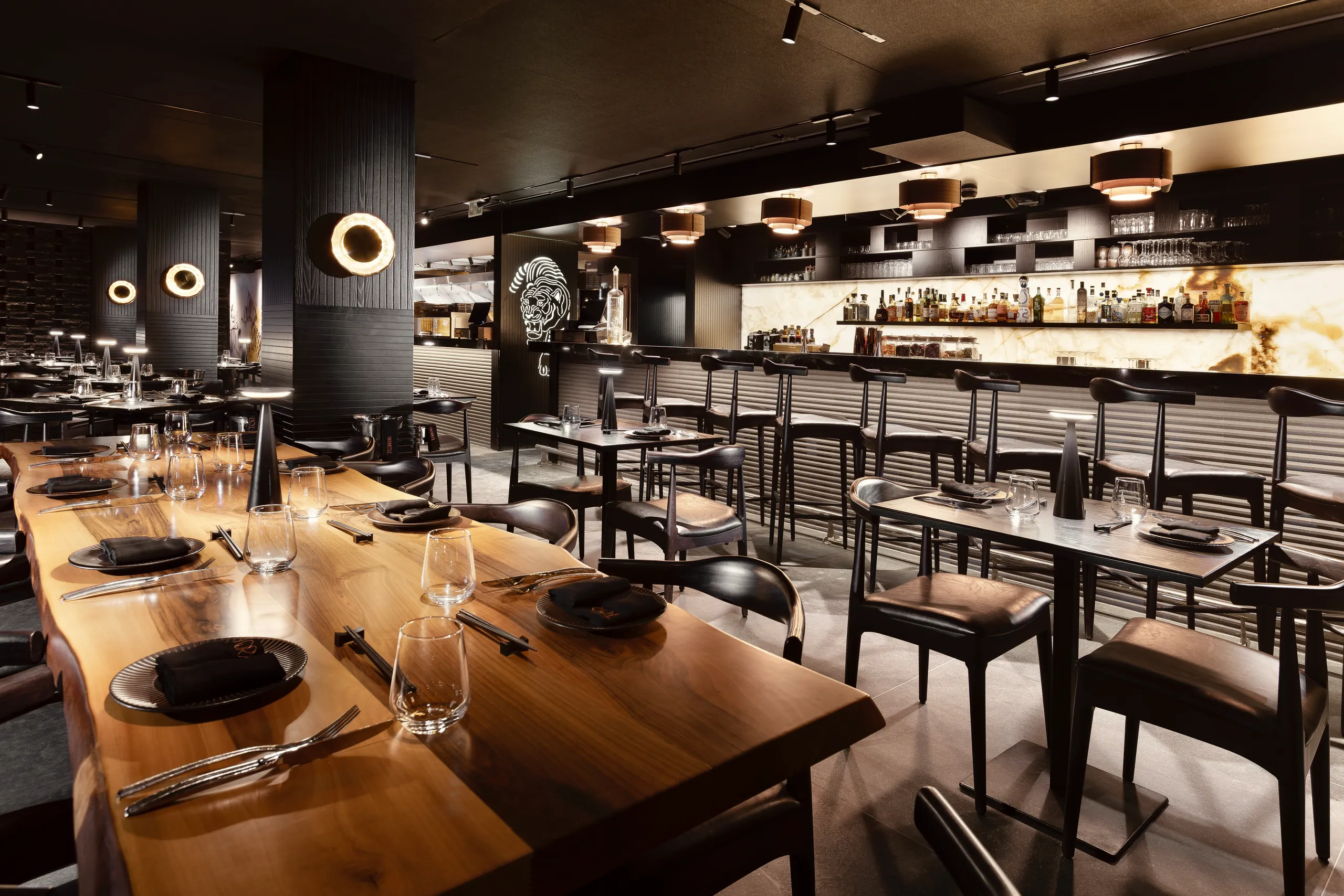 Long wooden table set for dinner with the lit bar behind