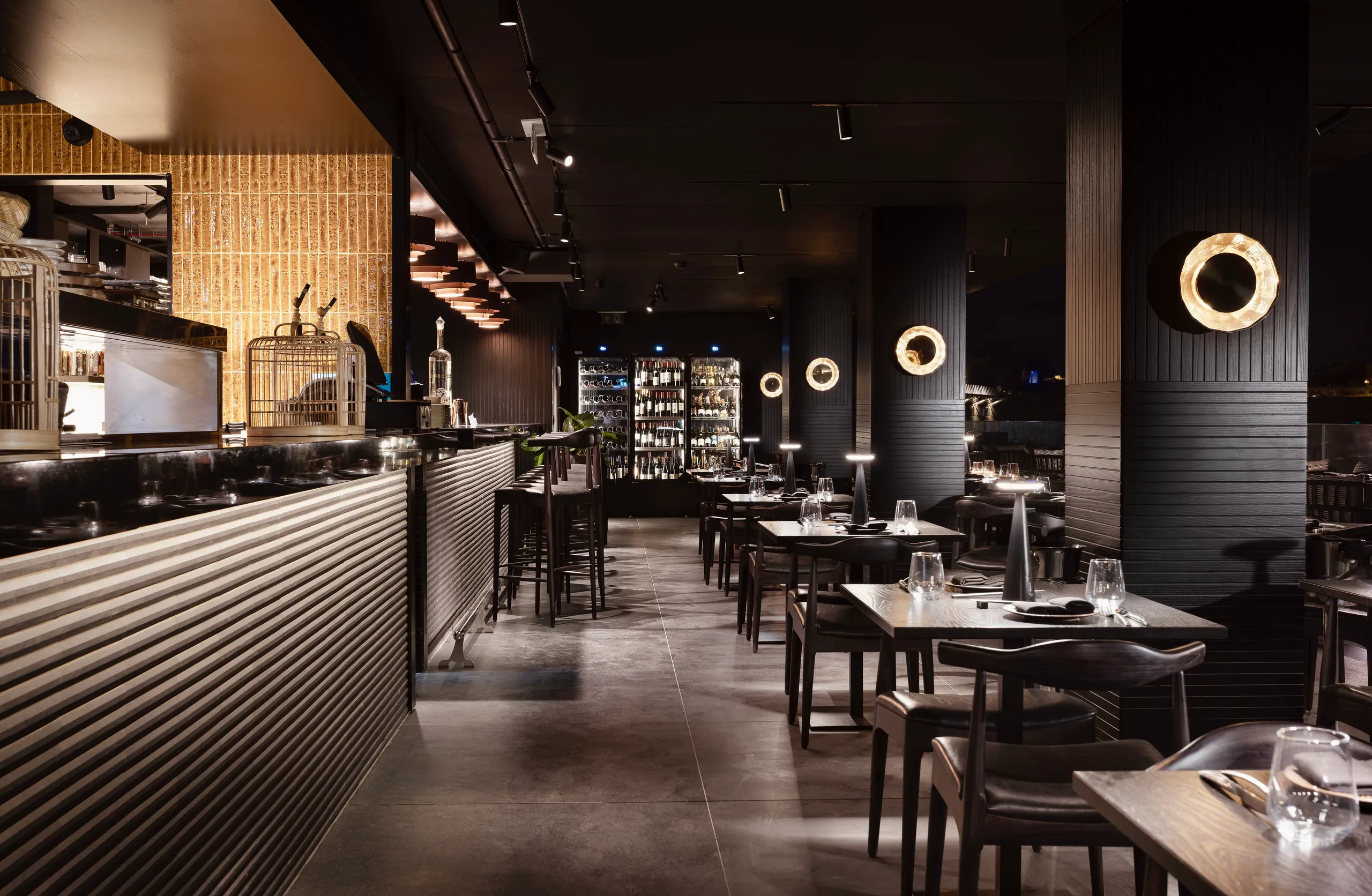 Dark dining room with black columns, round wall lights and a bar along the left