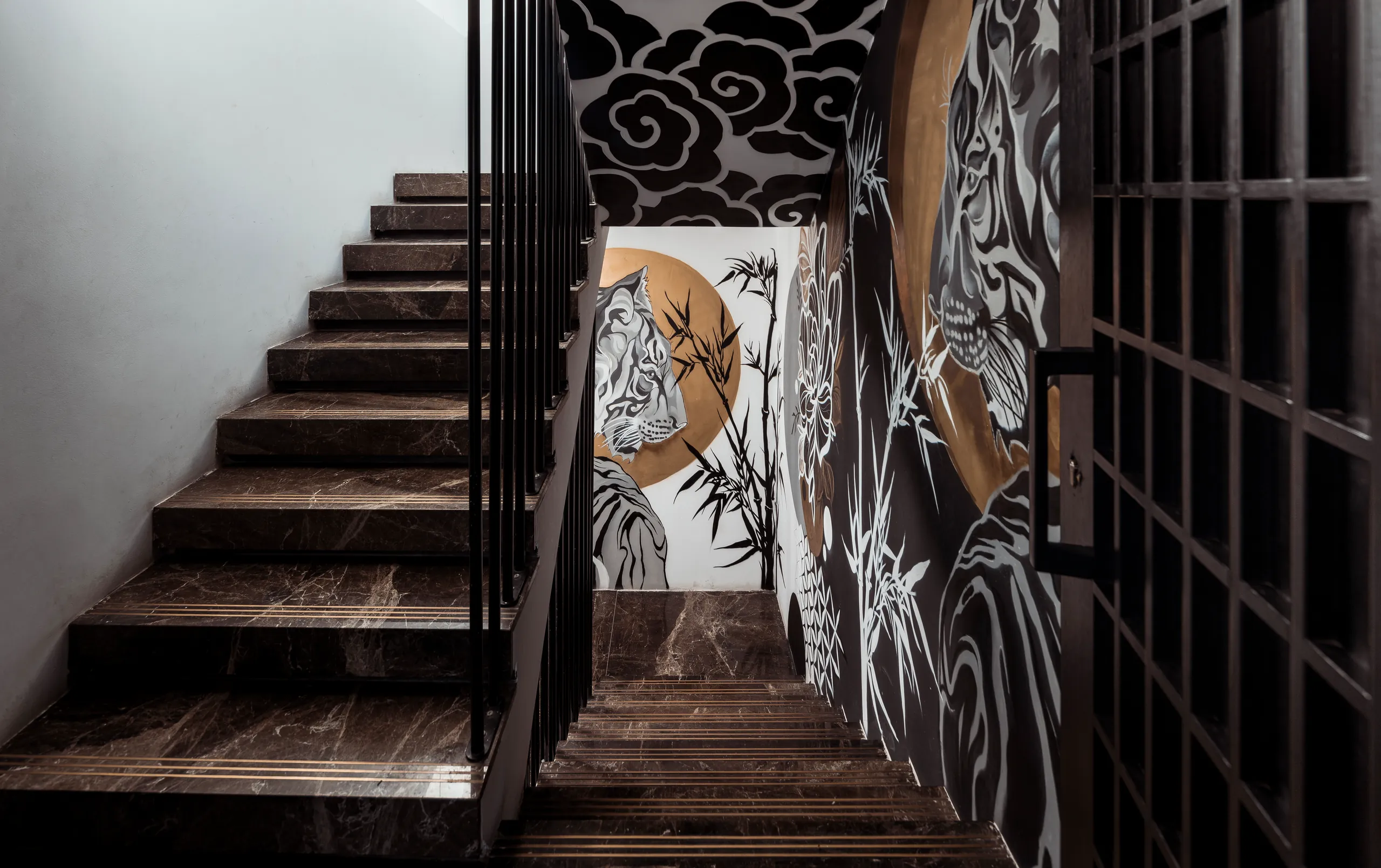 Wooden staircase beside a black-and-white wall mural of a tiger and bamboo