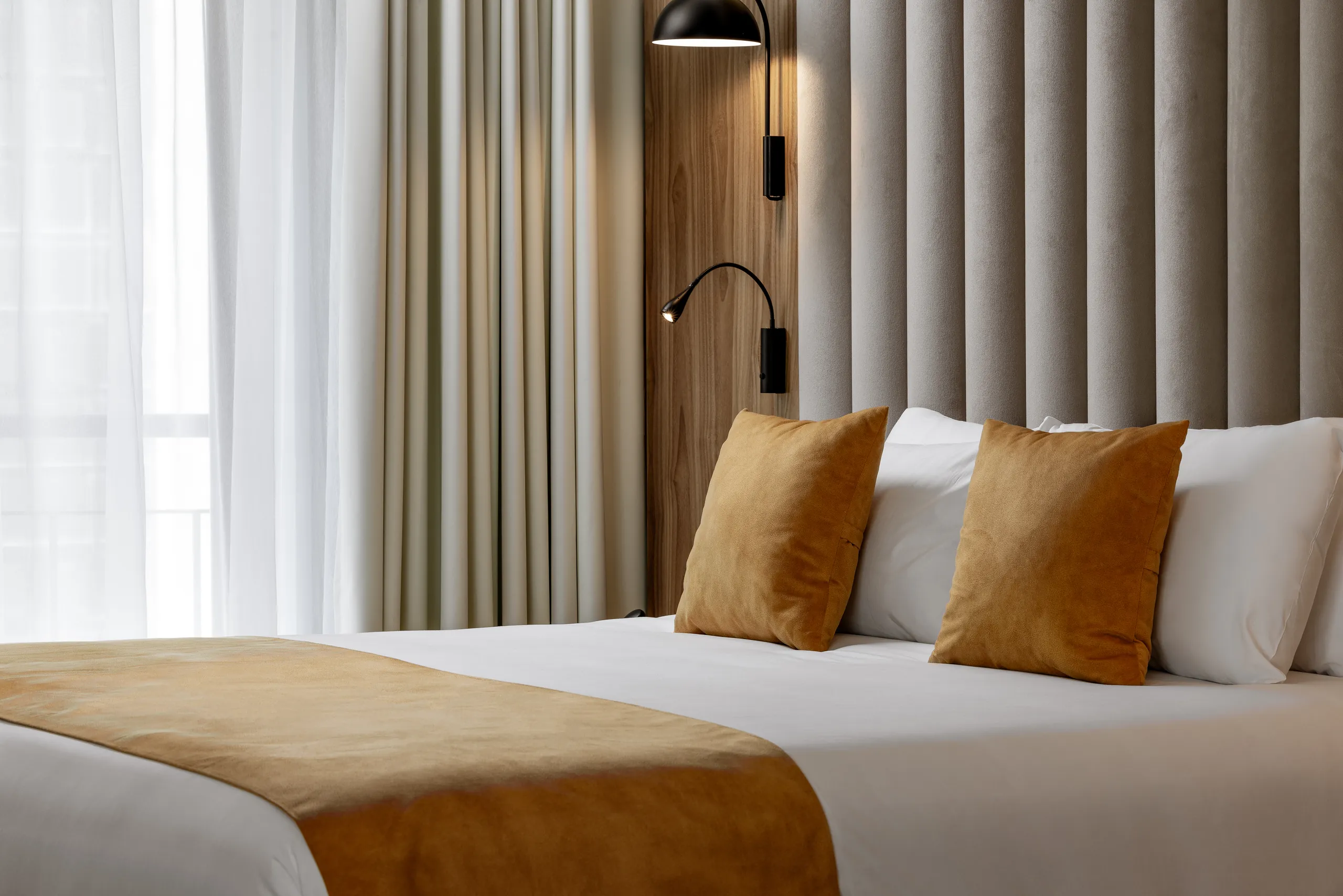 Double bed with mustard cushions and a throw against pale curtains