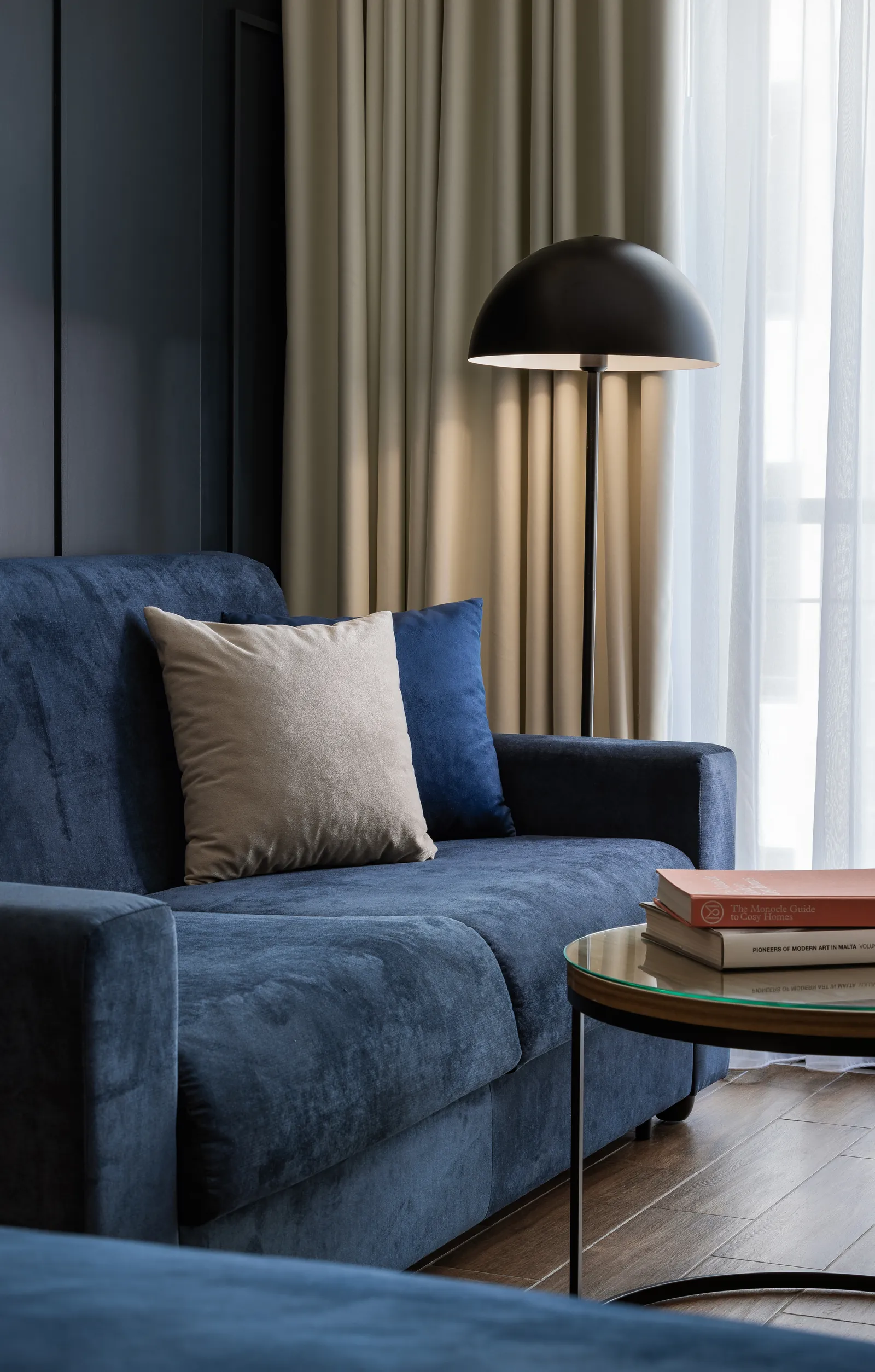 Blue sofa with cushions beneath a black pendant lamp and curtains