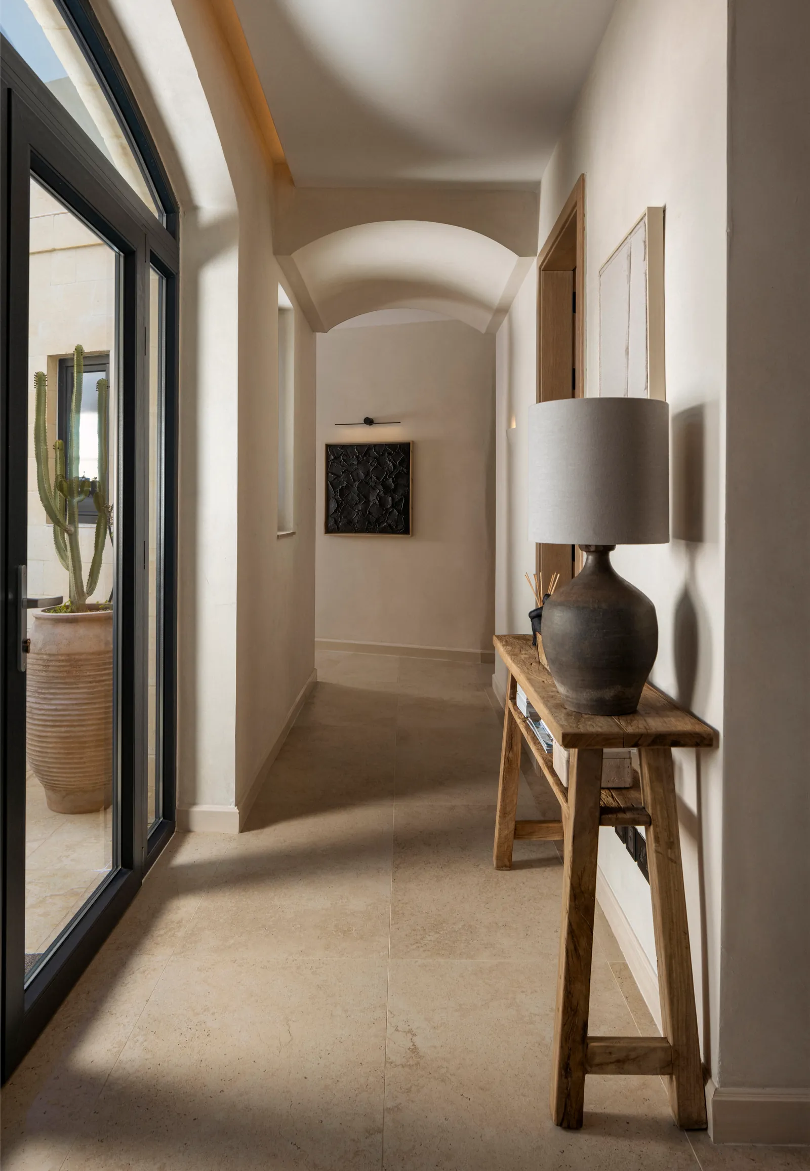 Hallway with a timber console, table lamp and framed art beside a glazed door