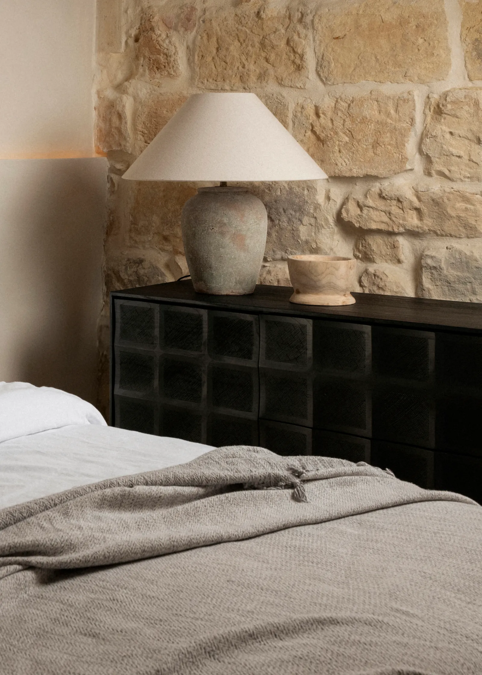 Table lamp on a black bedside cabinet against a limestone wall