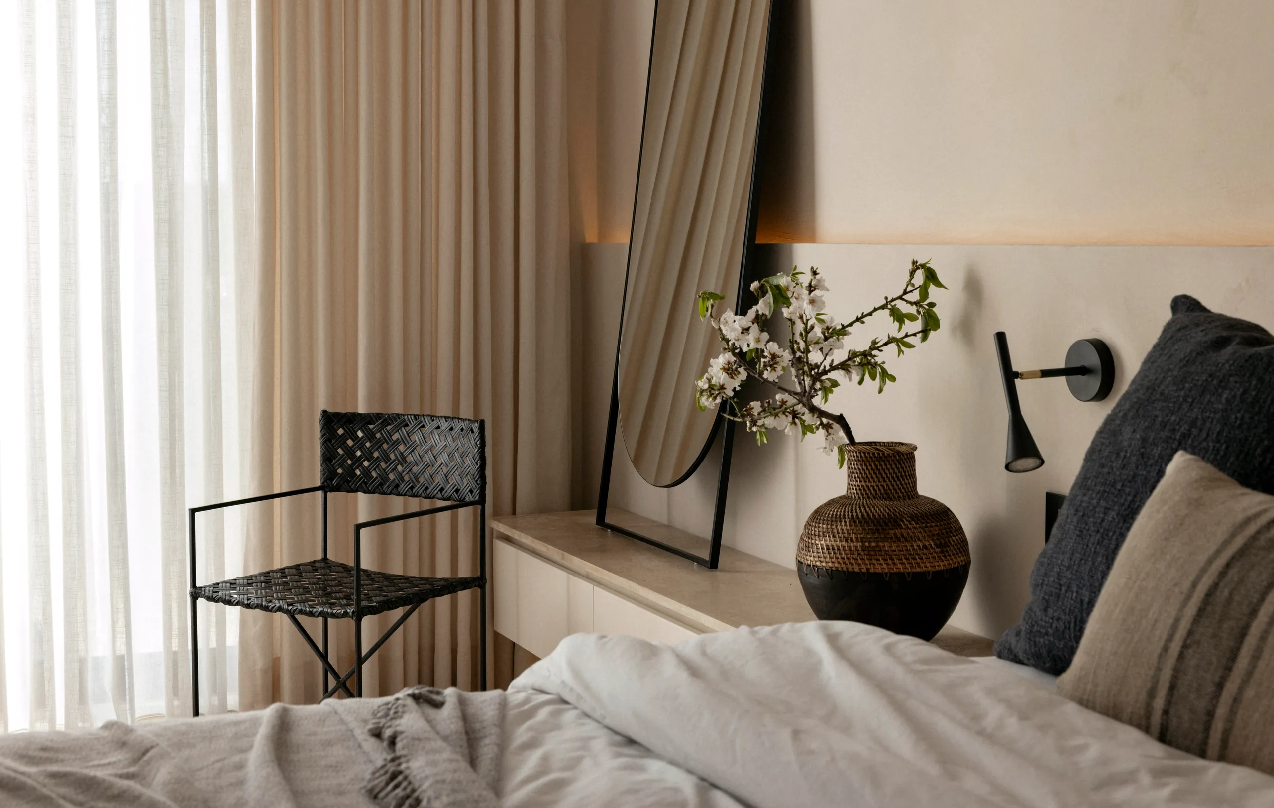 Bedroom corner with linen bedding, a black chair, blossom in a vase and sheer curtains