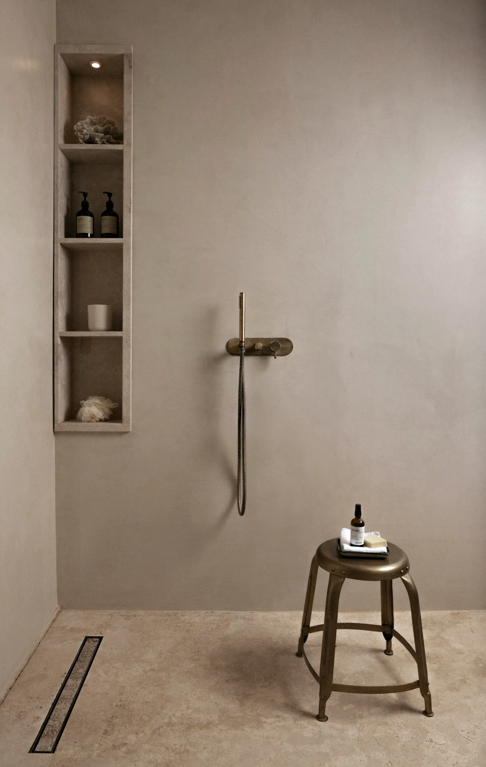 Minimal shower with a wall niche, linear drain and a small metal stool