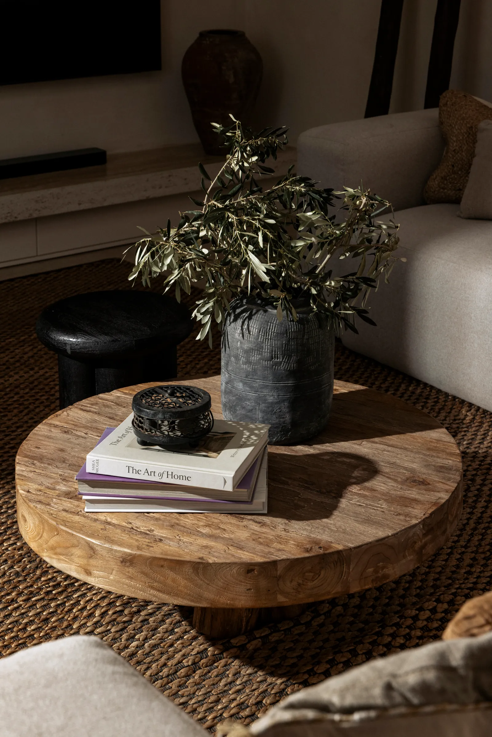 Olive branch in a stone vase on a round wooden coffee table with books
