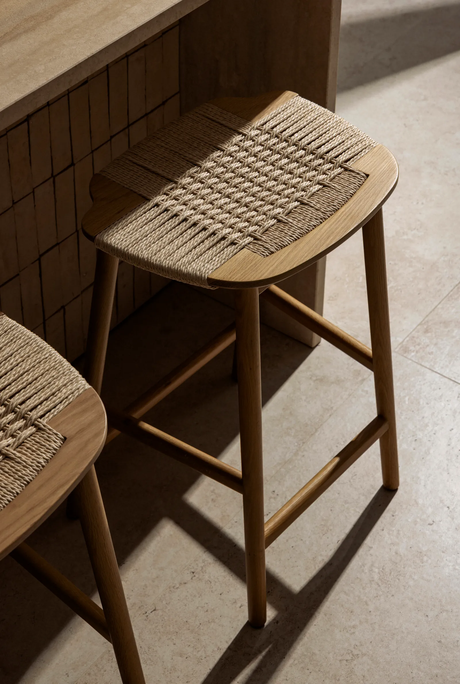 Woven-seat wooden bar stool beside a tiled wall
