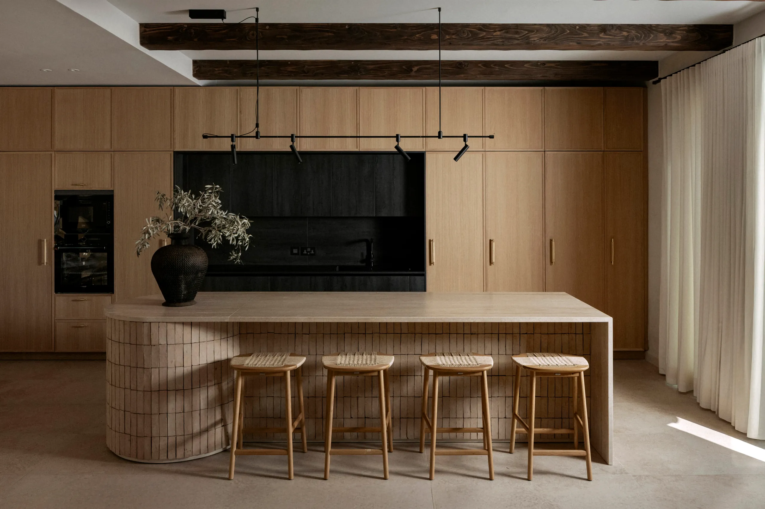 Oak kitchen with a tiled island, four stools and a dark wall-mounted cabinet